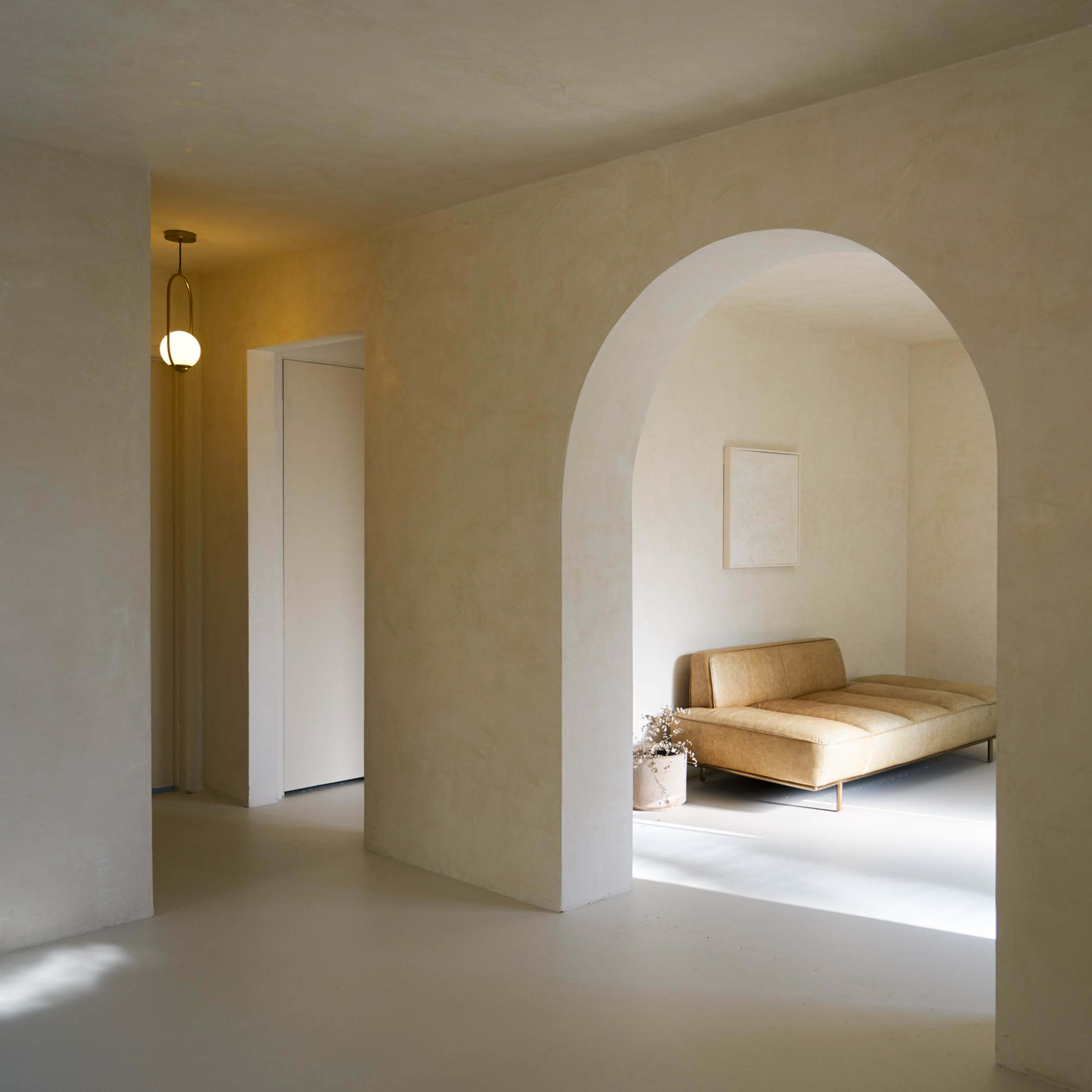 A minimalistic interior space featuring a light-colored archway, a beige sofa, and soft natural lighting.