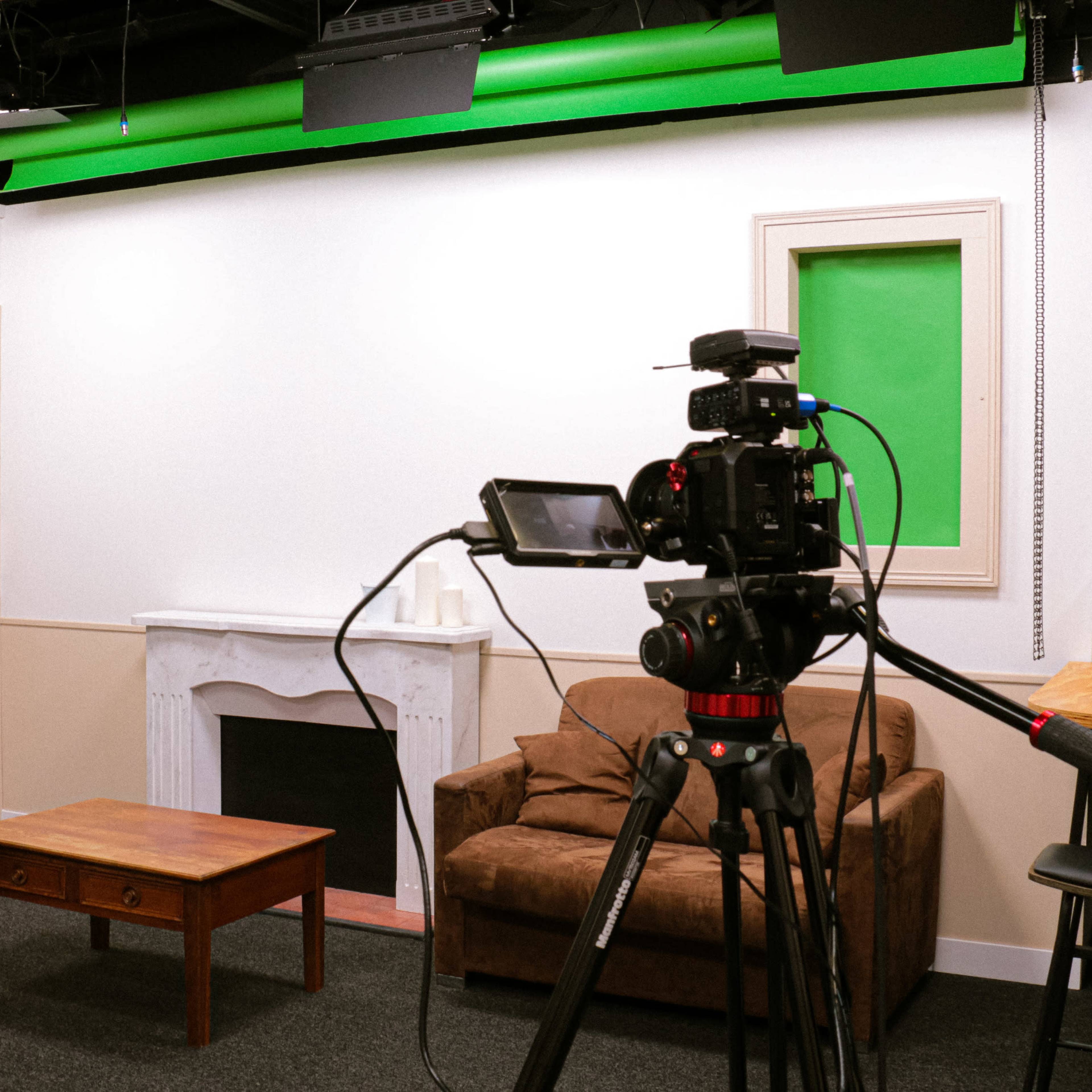 A studio setup with two cameras focused on a small living space featuring a brown couch, a wooden coffee table, and a green screen on the wall.