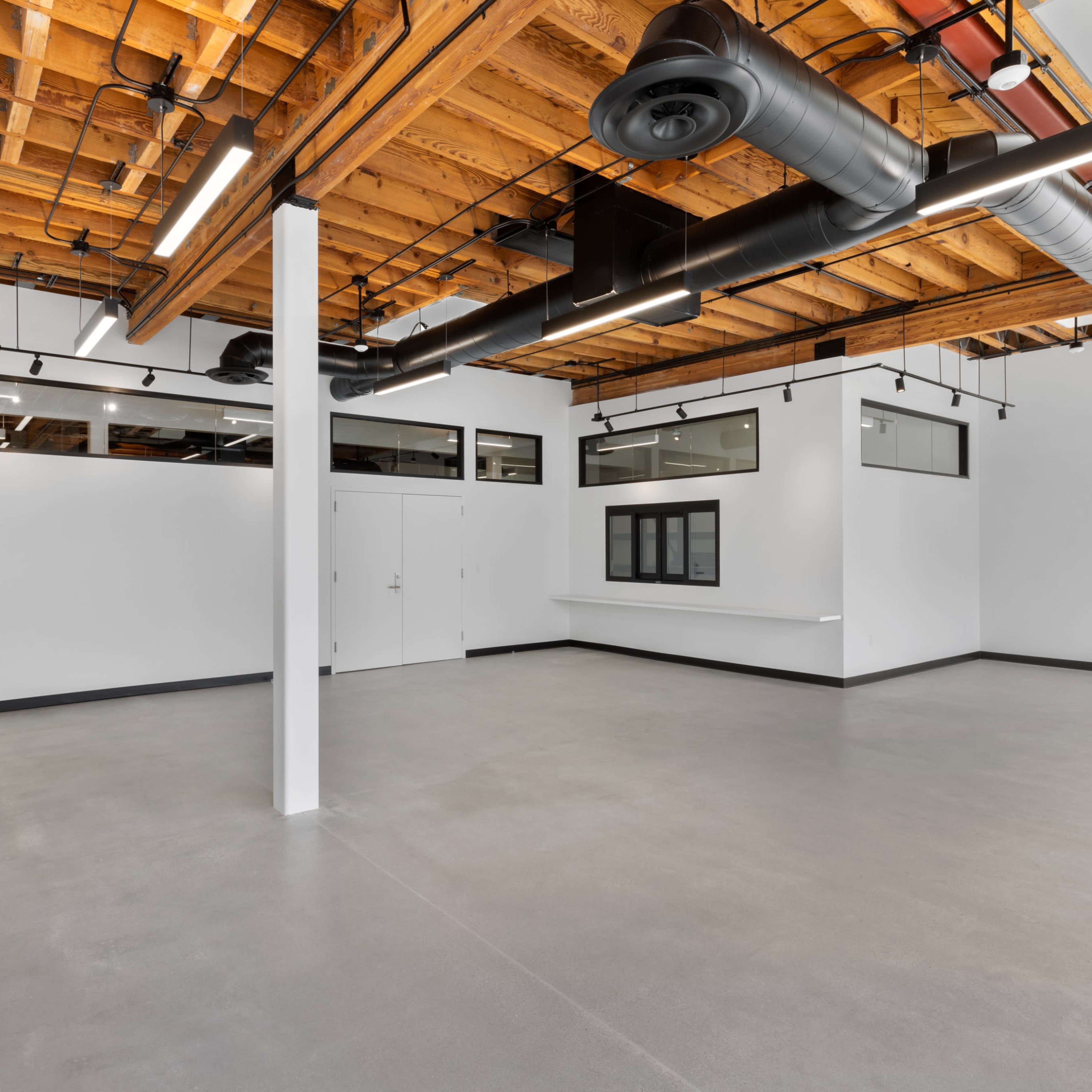 An empty room with a high wooden ceiling, grey concrete flooring, and large windows along the walls.