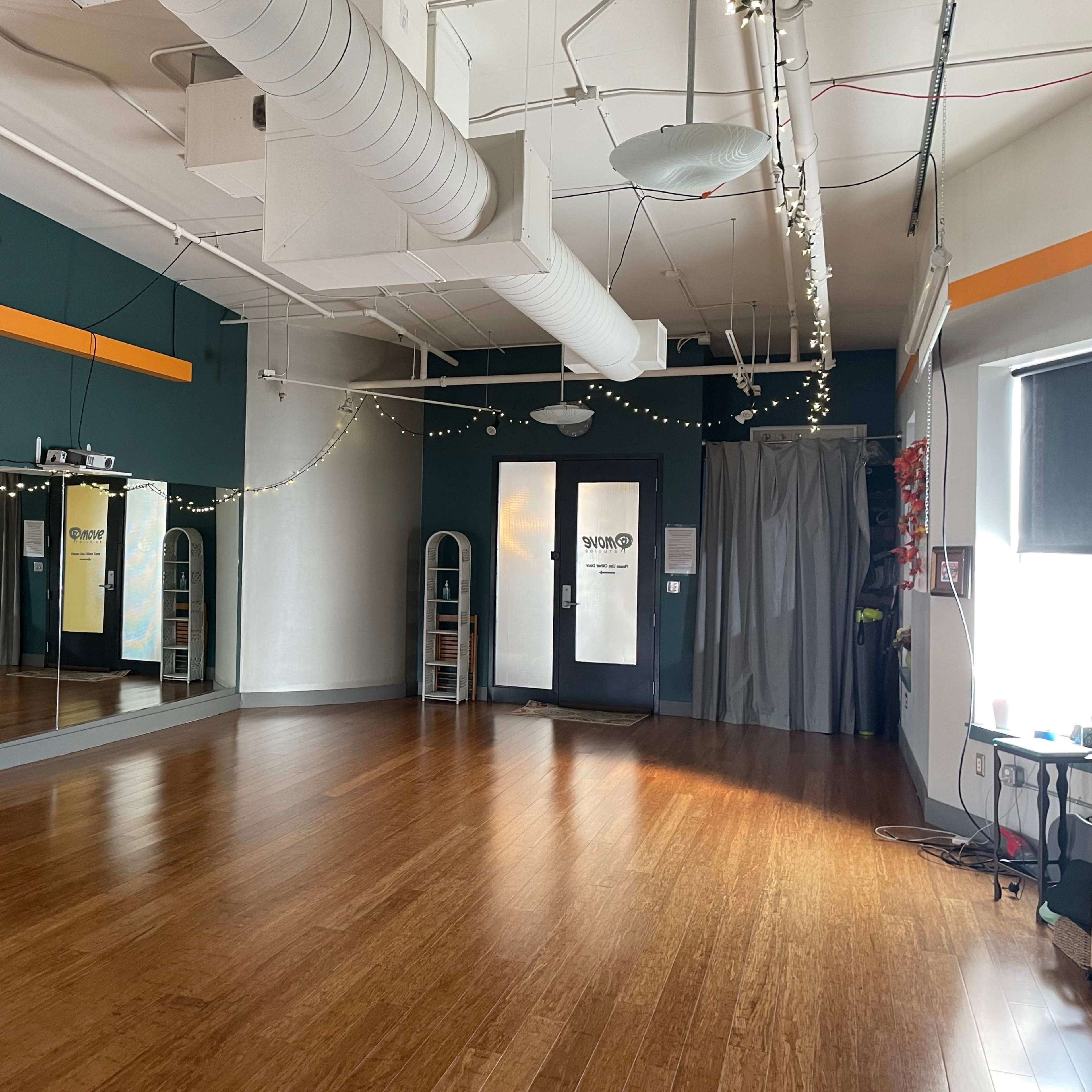 A spacious room with wooden flooring, green walls, a large mirror on one side, and a curtain-covered doorway on the other, decorated with string lights.