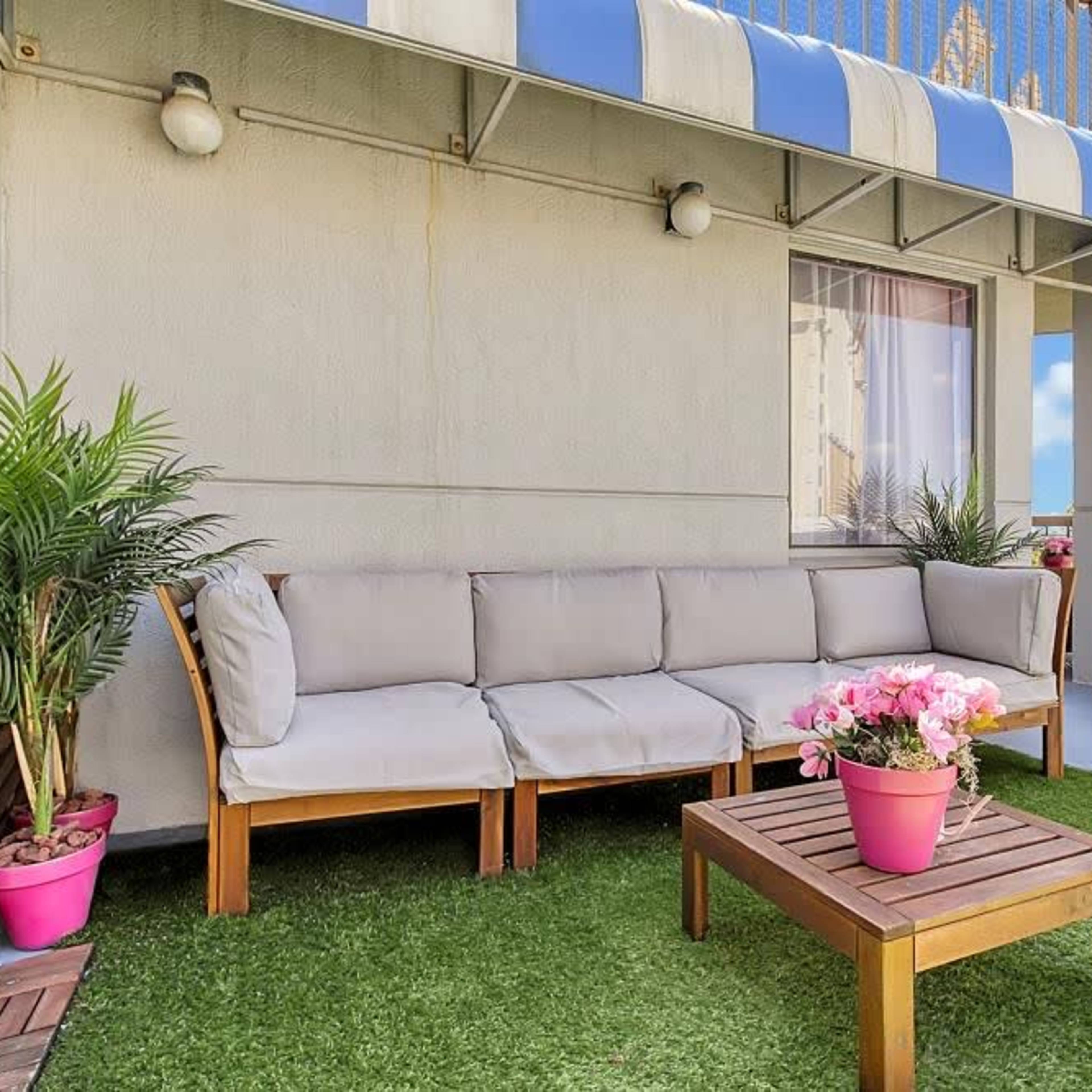 A balcony with a sofa set, a wooden coffee table, and potted plants on green artificial grass.