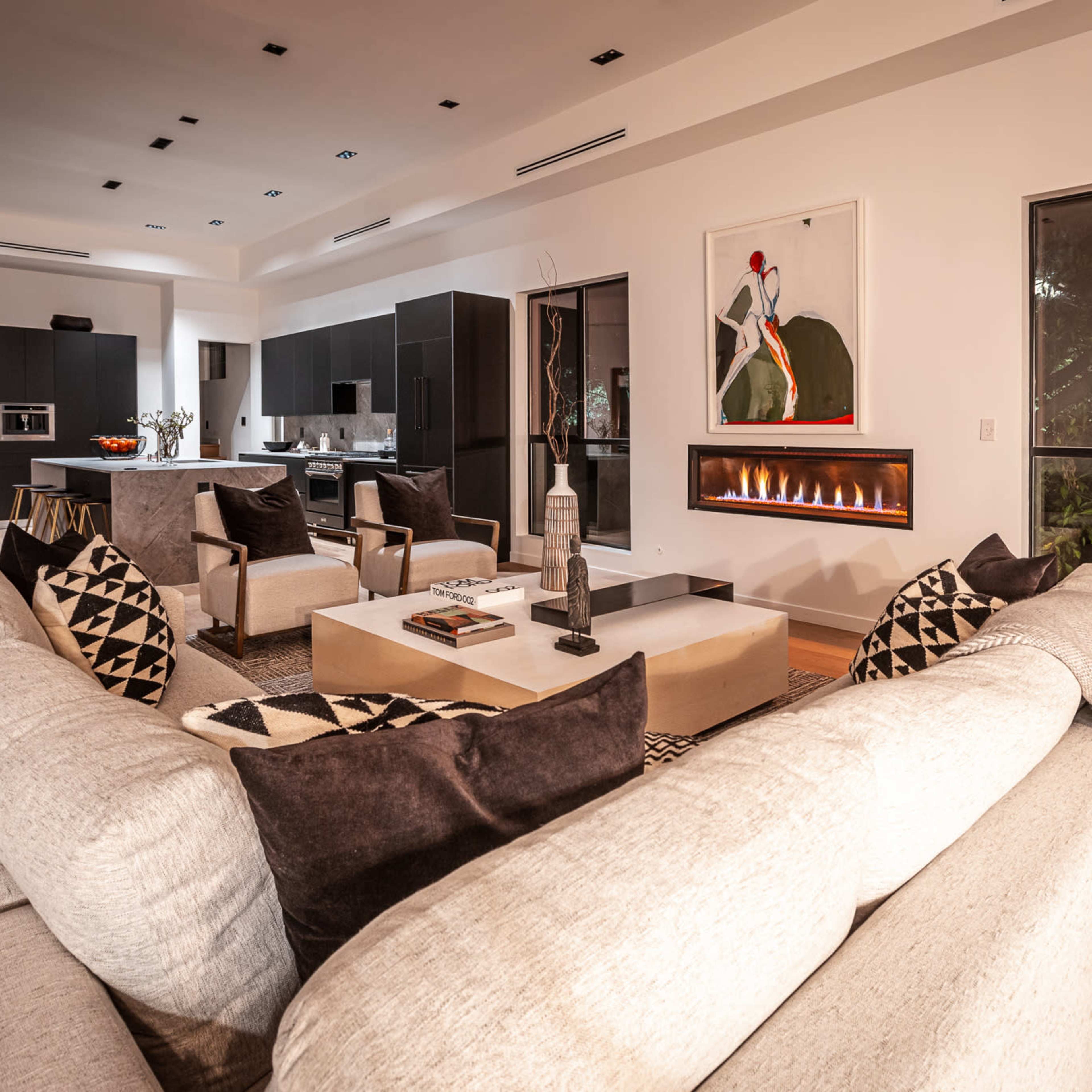 A modern living room with a large sectional sofa facing a fireplace and an open kitchen in the background.