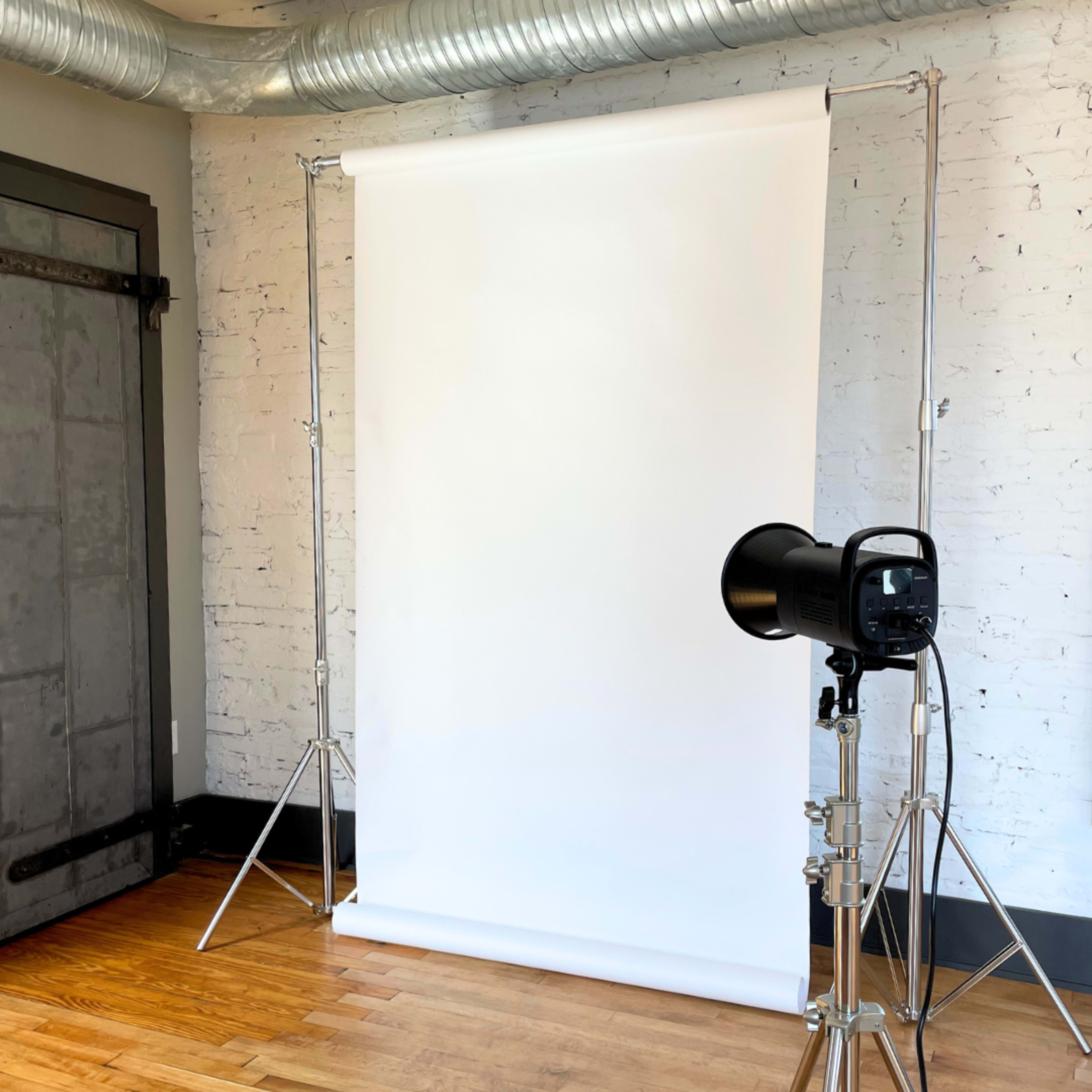 A spacious room with hardwood floors, featuring large windows, a decorative hanging light fixture, and a wall adorned with abstract line art.
