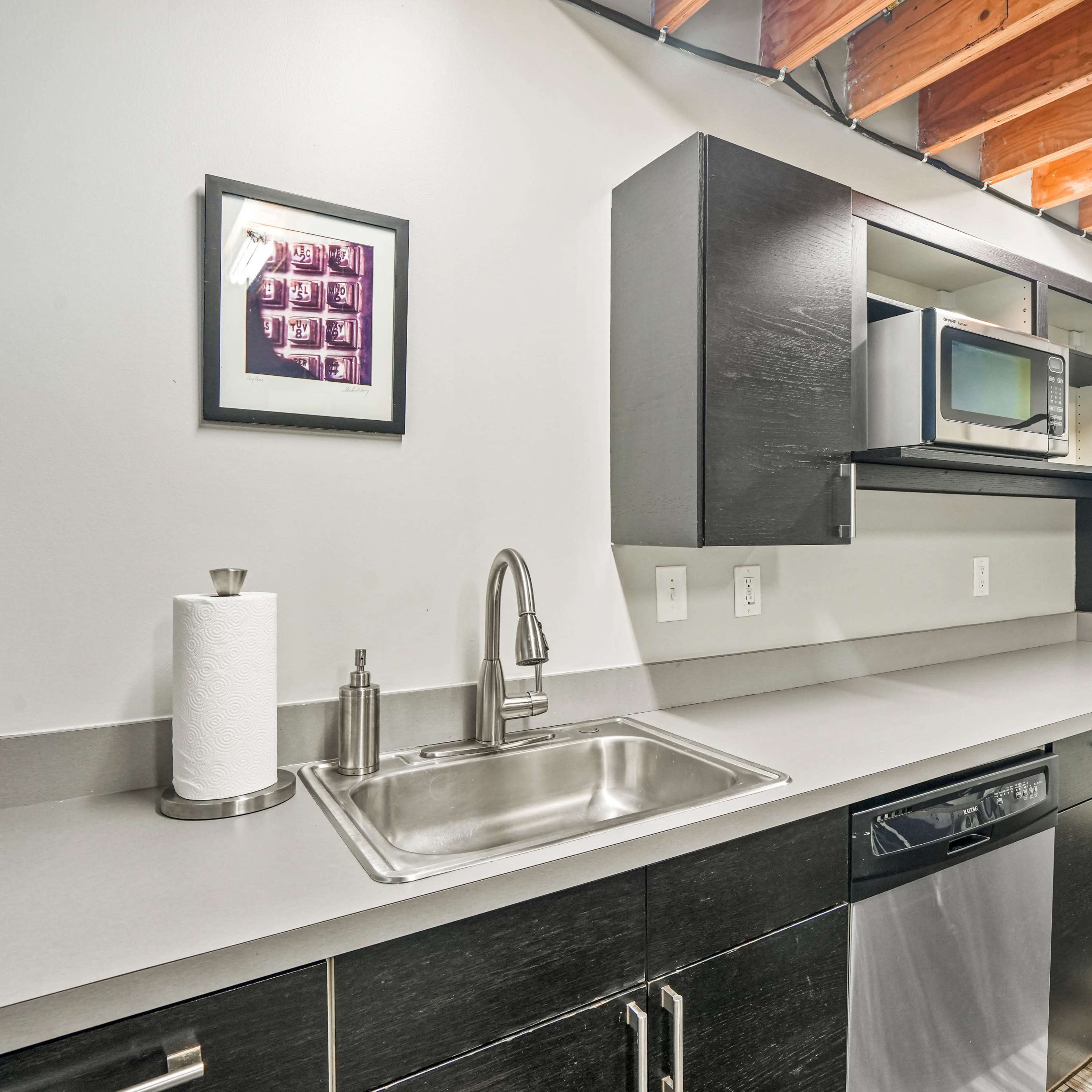 A modern kitchen with dark cabinetry, a stainless steel sink, and an integrated microwave above the countertop.