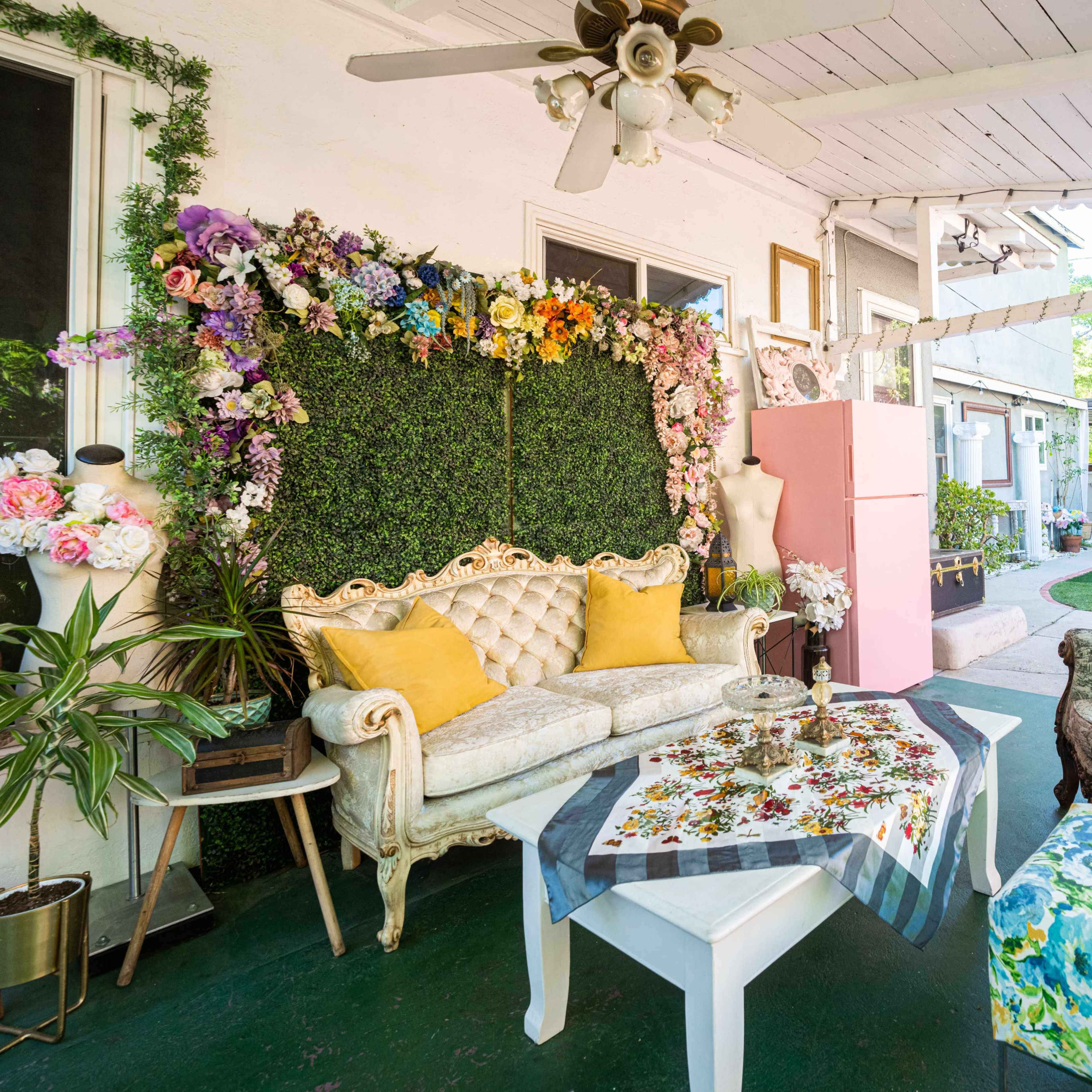 A patio area with a floral backdrop, vintage furniture, and decorative elements arranged around a table.
