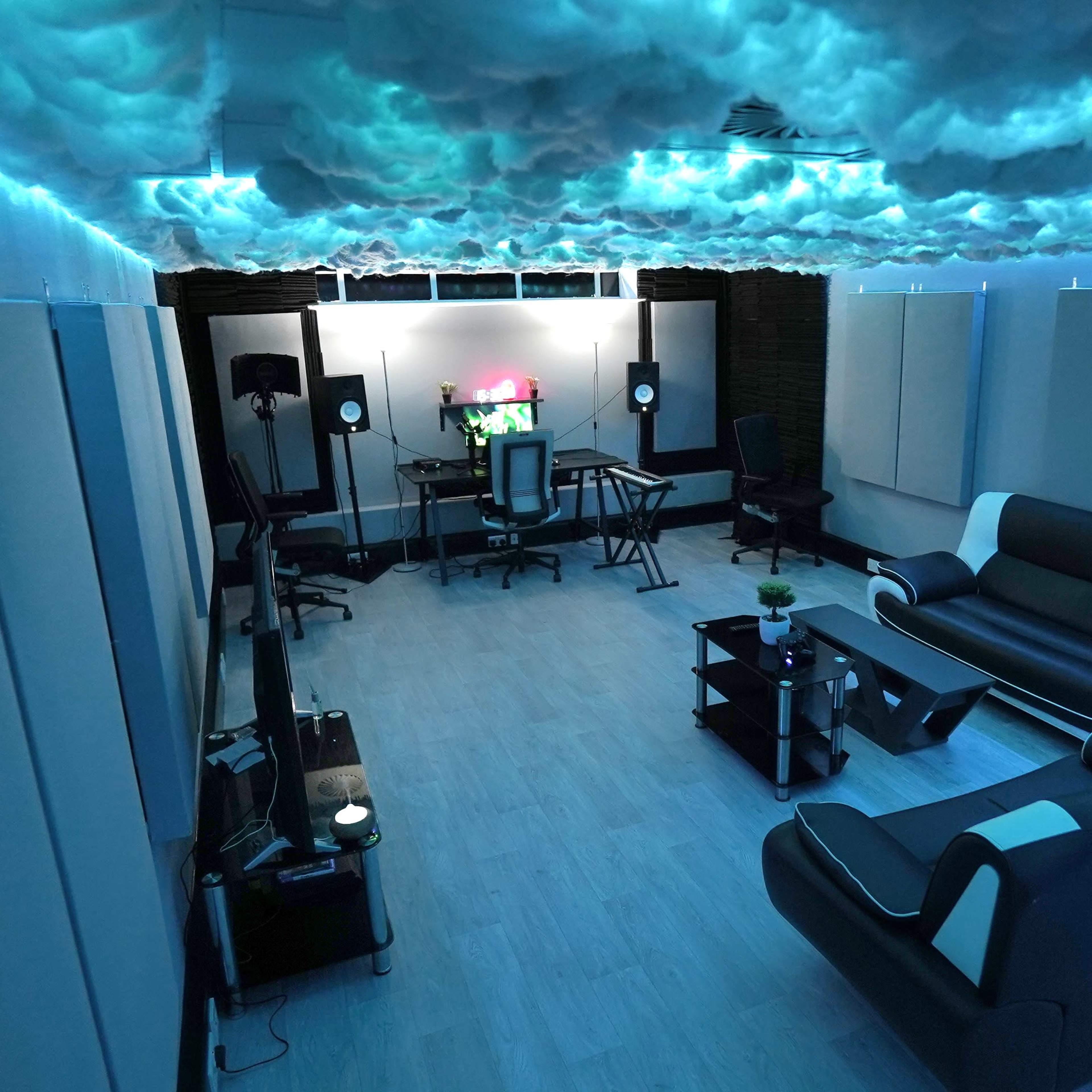 A modern studio room with a cloud-themed ceiling, comfortable seating, and sound equipment set up against the walls.