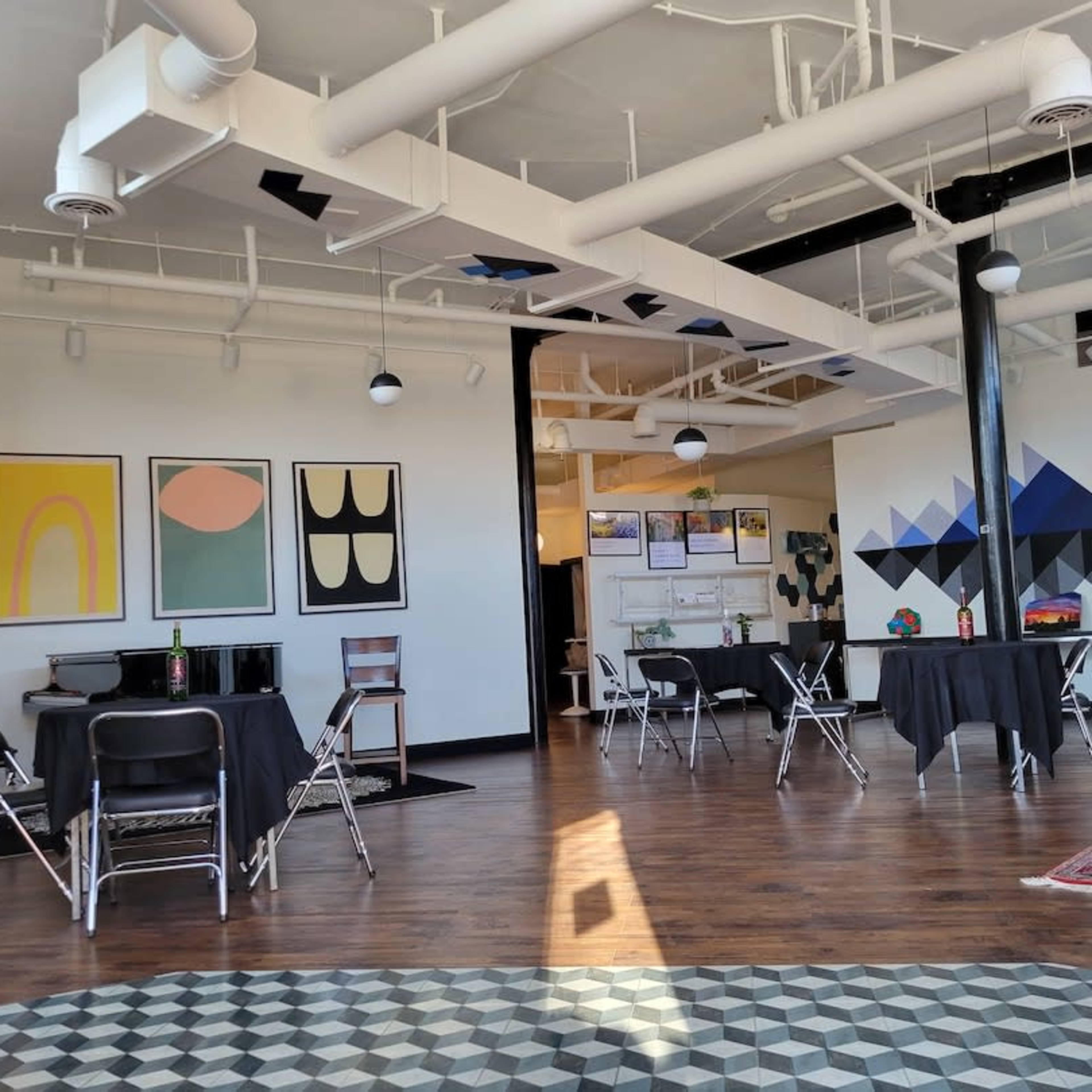 A spacious room with several tables covered in black cloth, surrounded by artwork on the walls and patterned flooring.