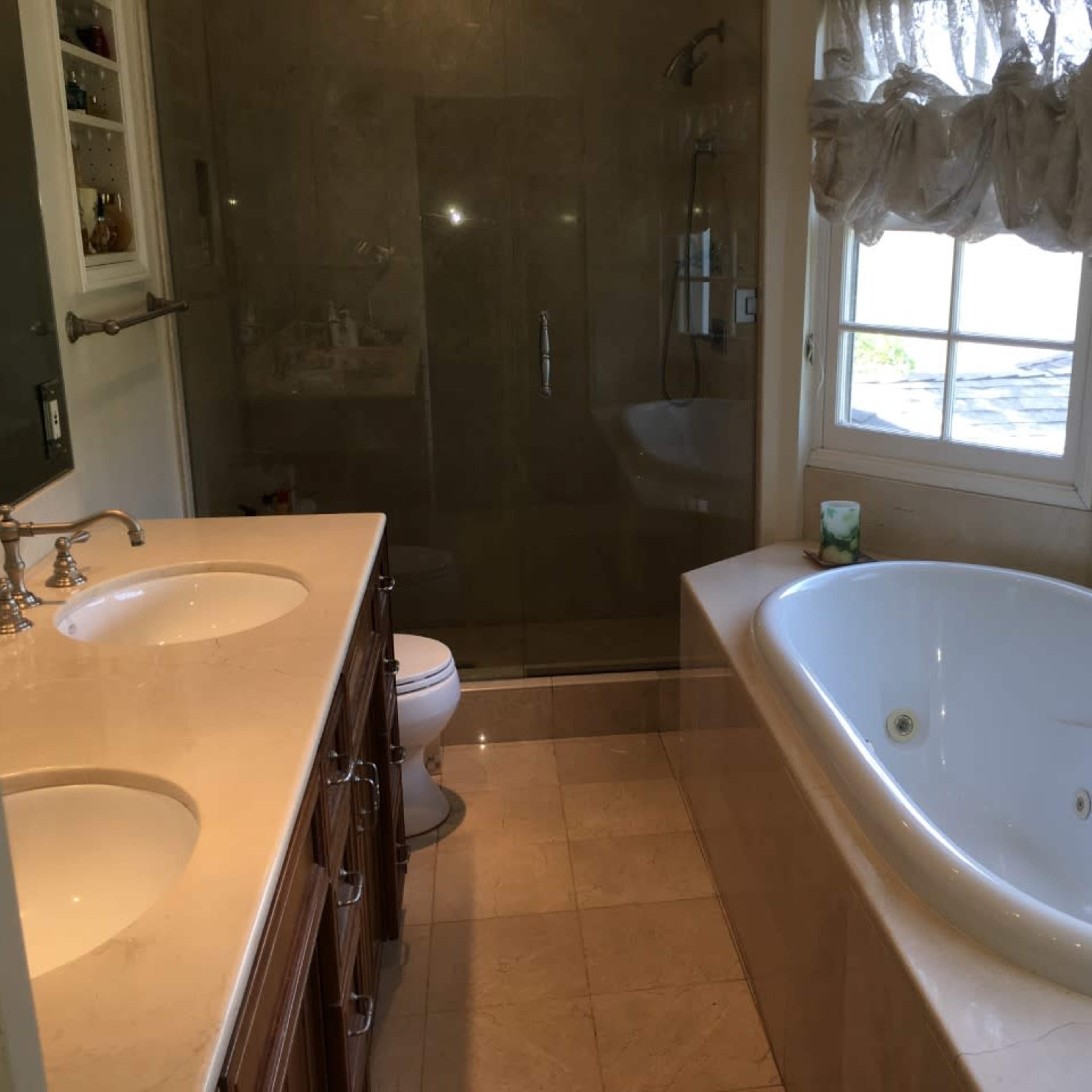 A bathroom features a double vanity with sinks, a glass-enclosed shower, a freestanding bathtub, and large windows with sheer curtains.