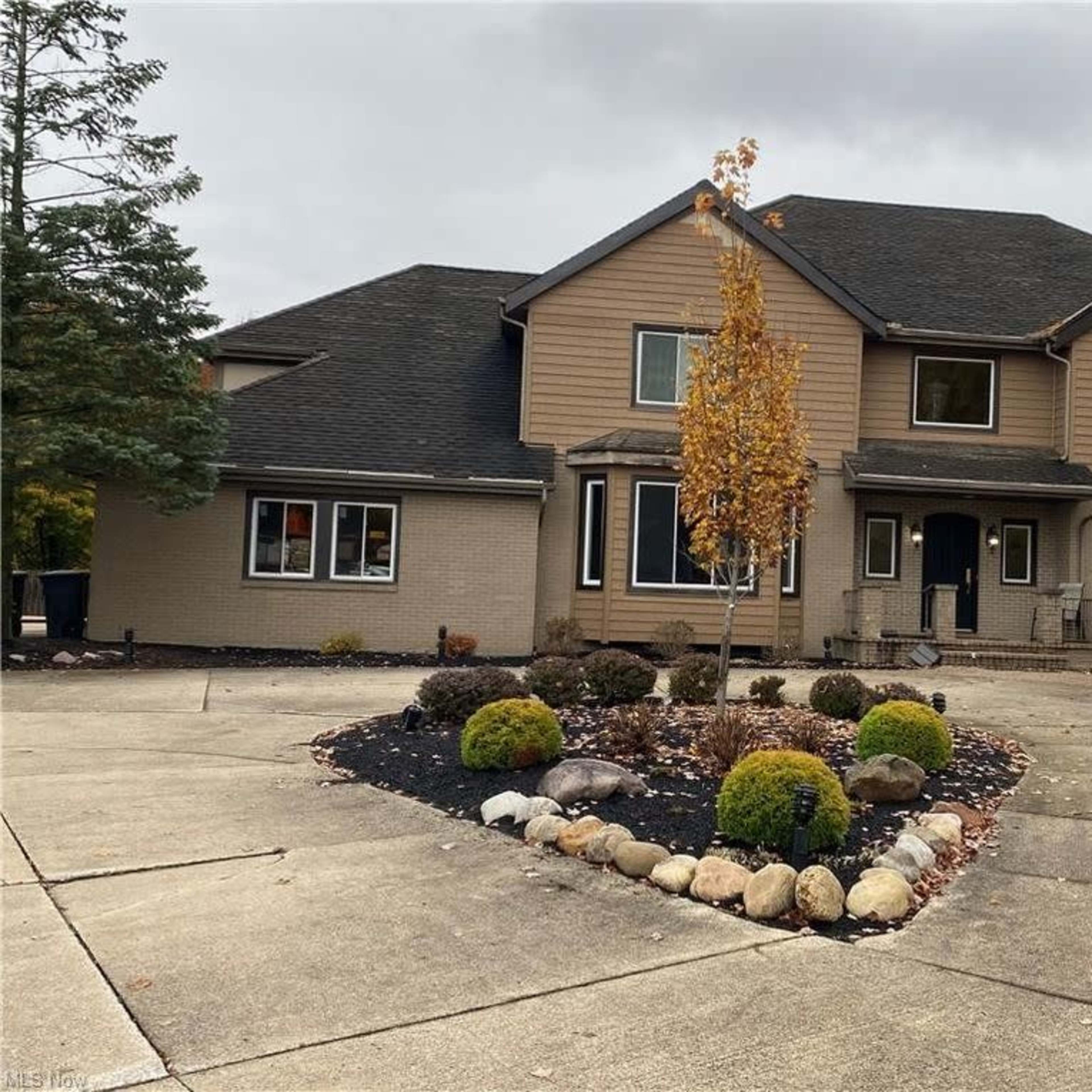 A large, two-story house with a brown and beige exterior, featuring landscaped grounds and a circular driveway.