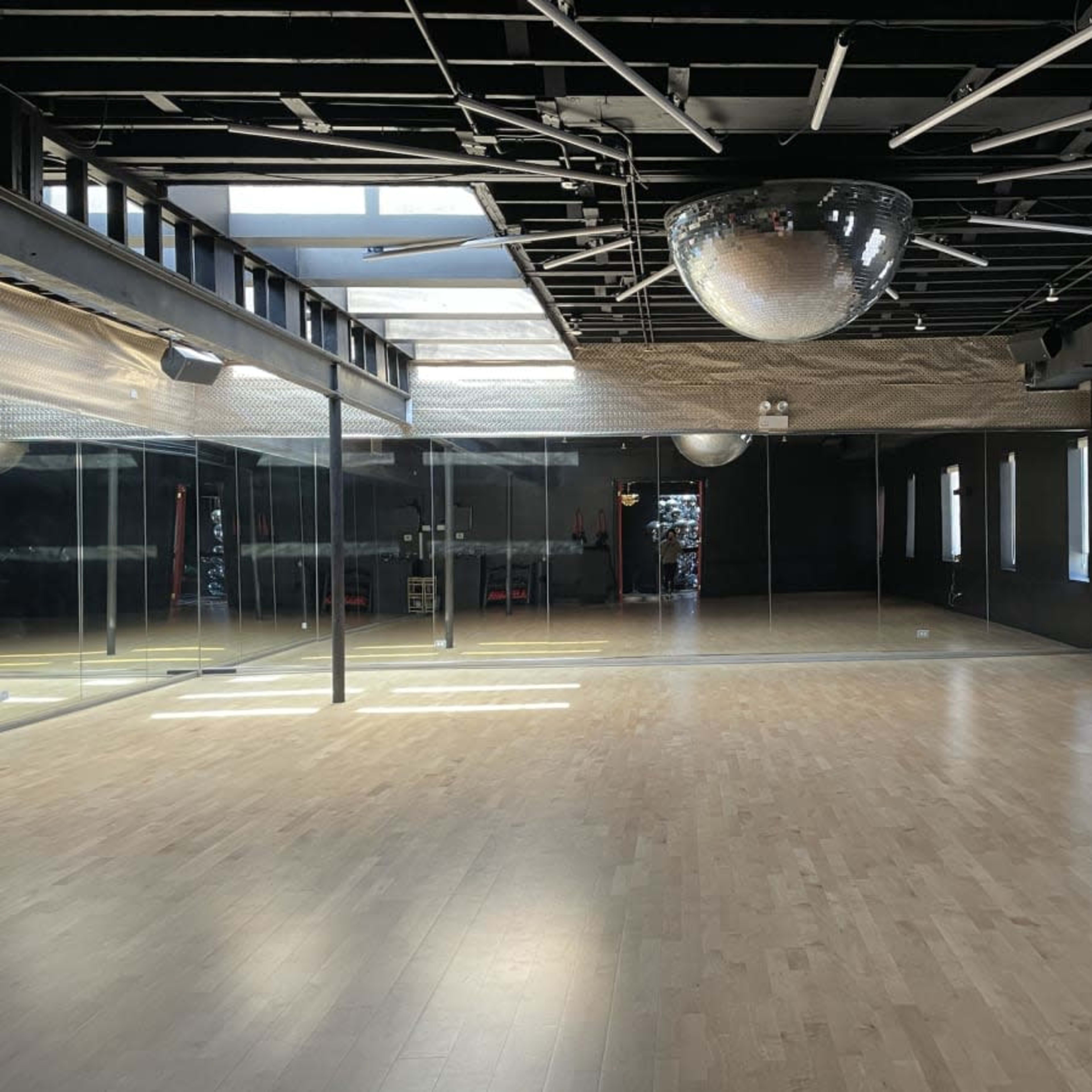 An empty dance studio with a large mirror wall, wooden floor, and a disco ball hanging from the ceiling.