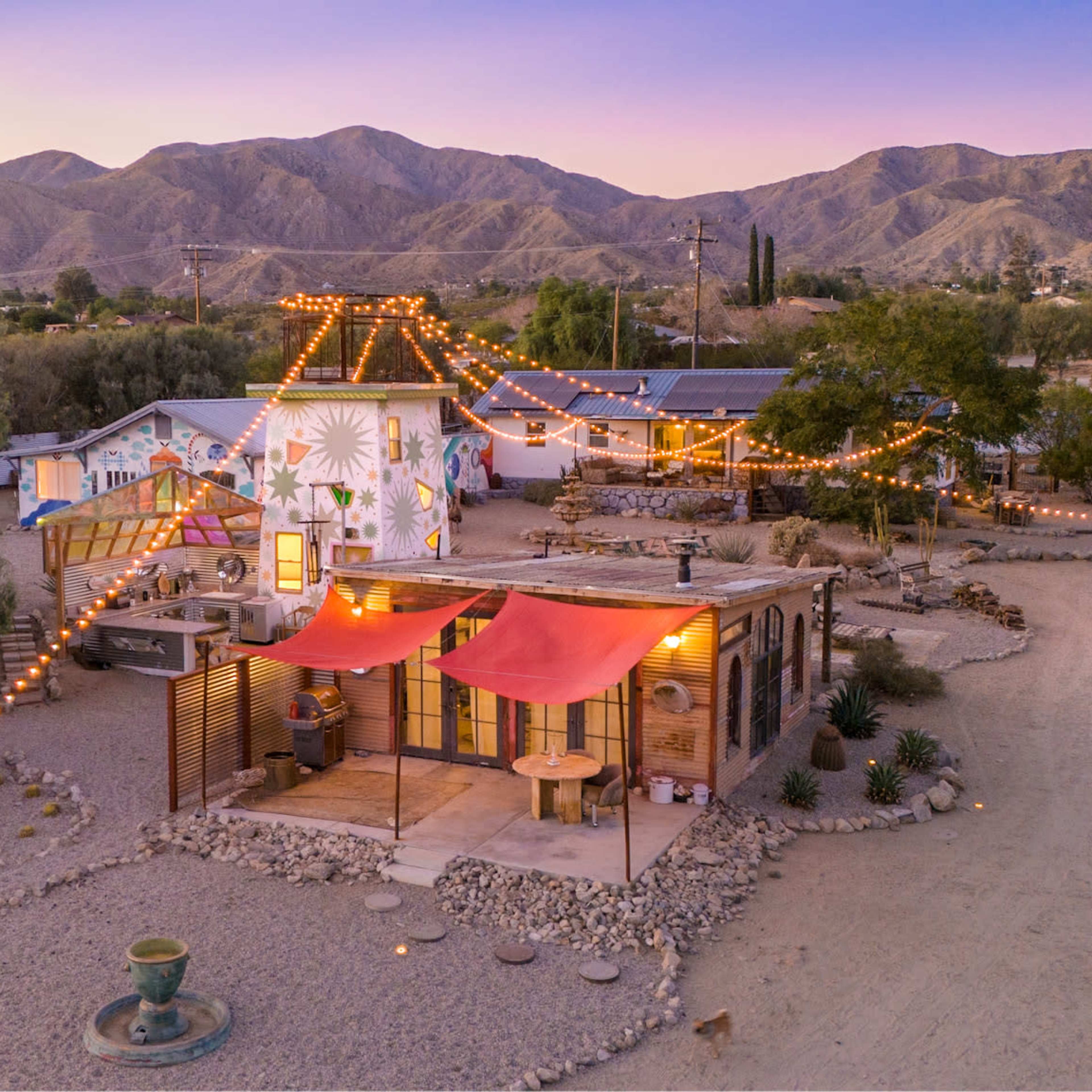 A colorful house with string lights is surrounded by desert landscaping and mountains in the background.