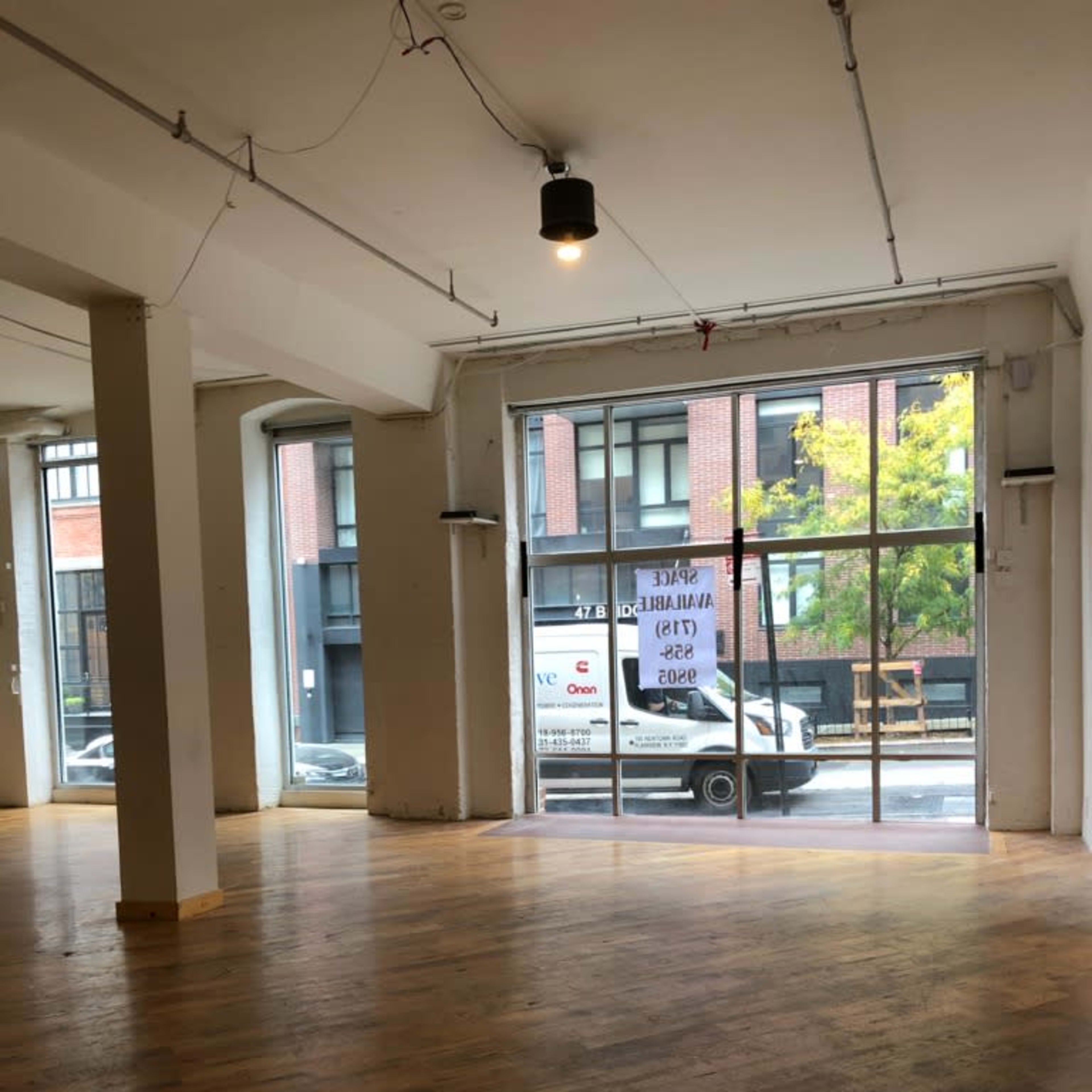 An empty interior space with wooden floors and large glass windows facing a street where a truck is parked outside.