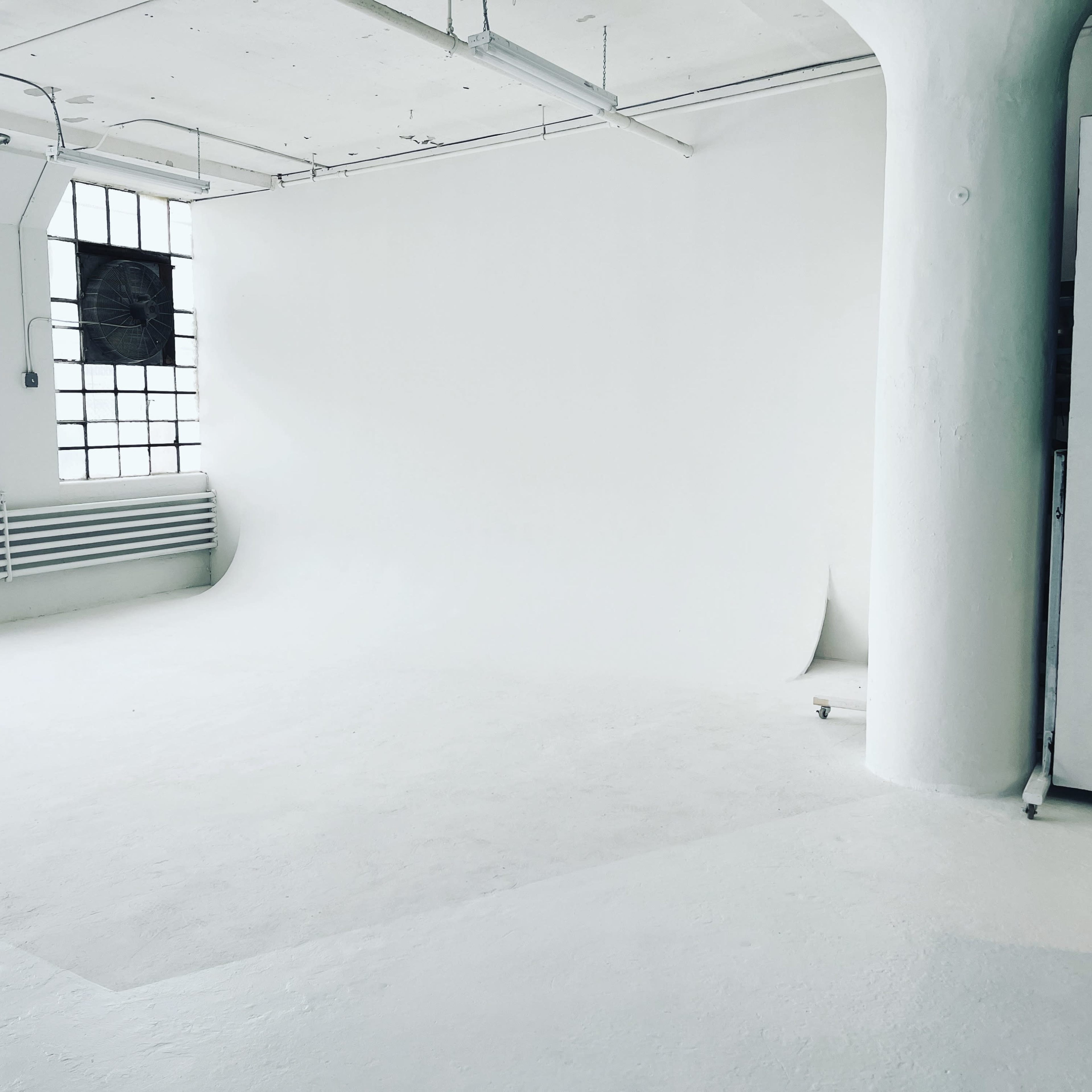 A spacious, empty studio featuring white walls, a white backdrop, and large windows.