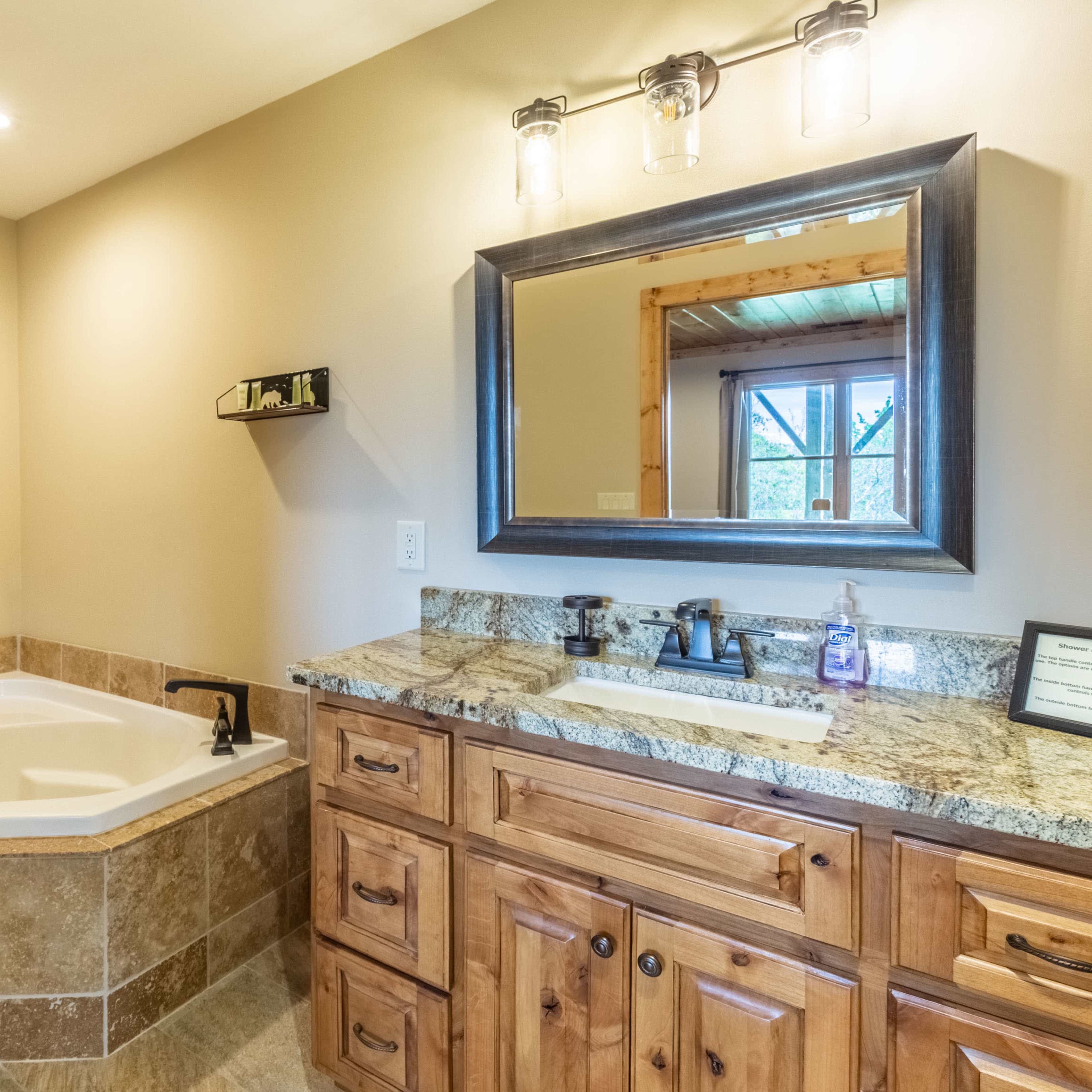 A bathroom featuring a jetted tub, a wooden vanity with a granite countertop, and a mirror above the sink.