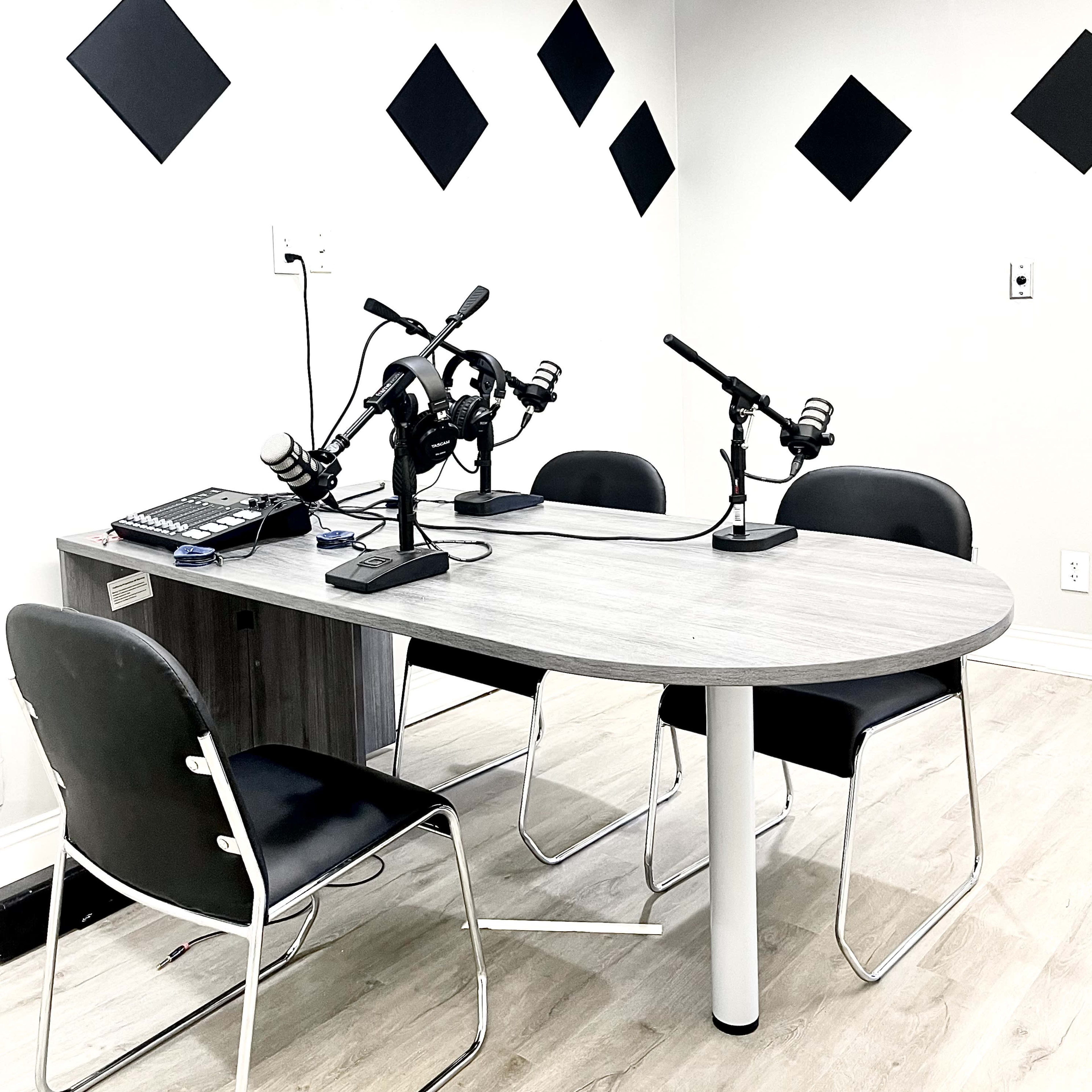 A modern podcast studio with a table, four chairs, and three microphones set up on the table.