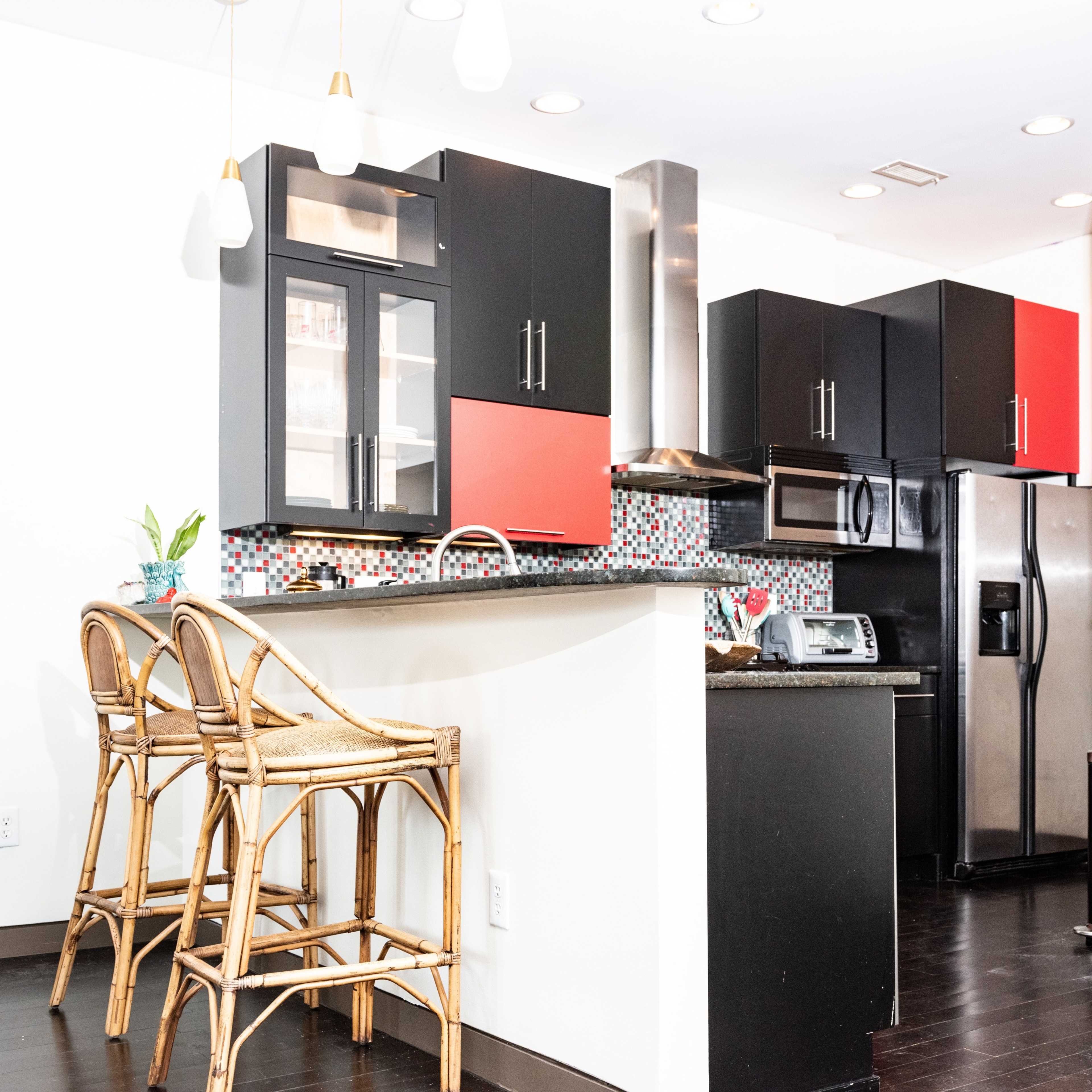 A modern kitchen with black and red cabinetry, a bar area with three rattan stools, and stainless steel appliances.