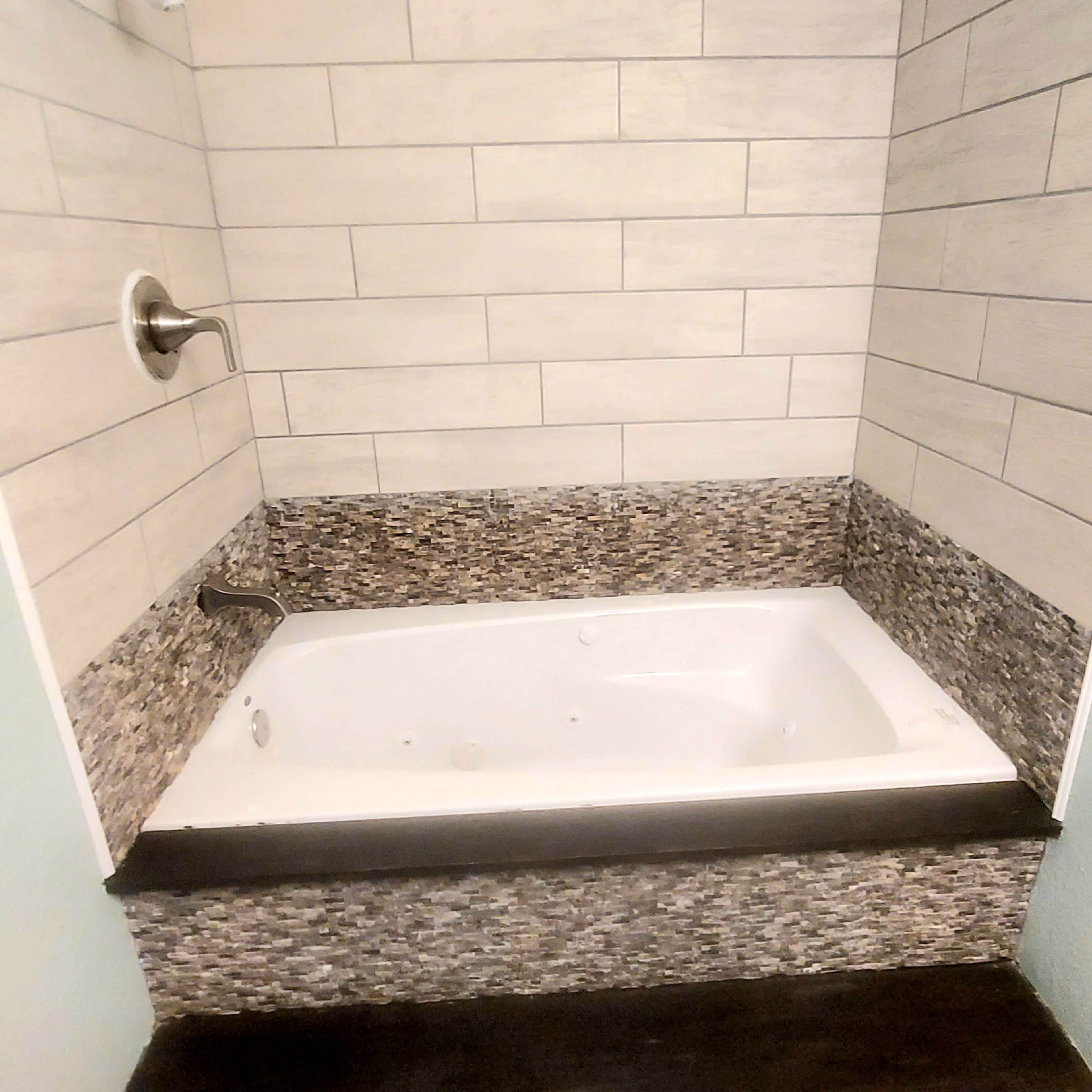 A corner bathtub enclosed by tiled walls with a stone accent base.