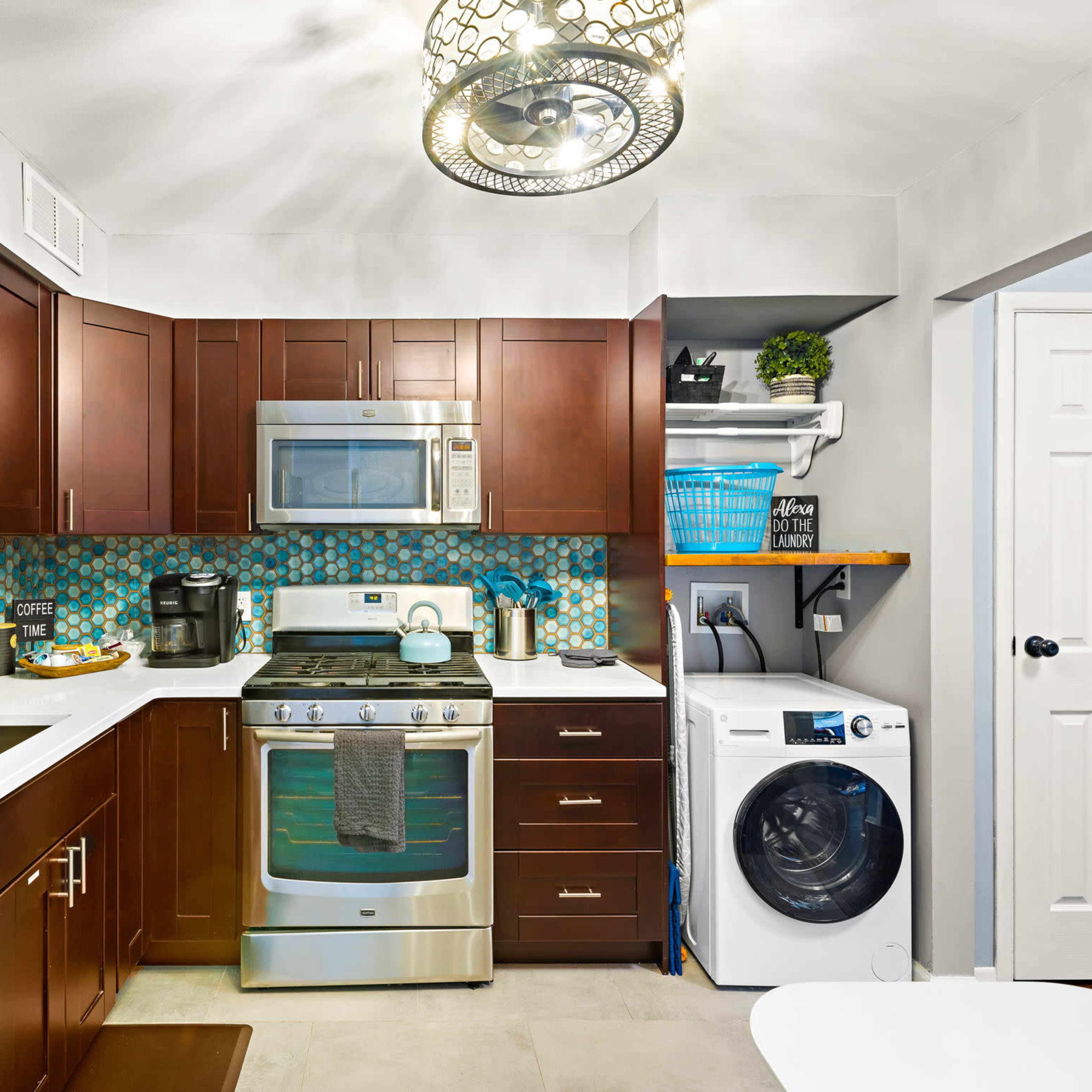 A modern kitchen features dark wood cabinets, stainless steel appliances, a tile backsplash, and a washer and dryer integrated into the cabinetry.