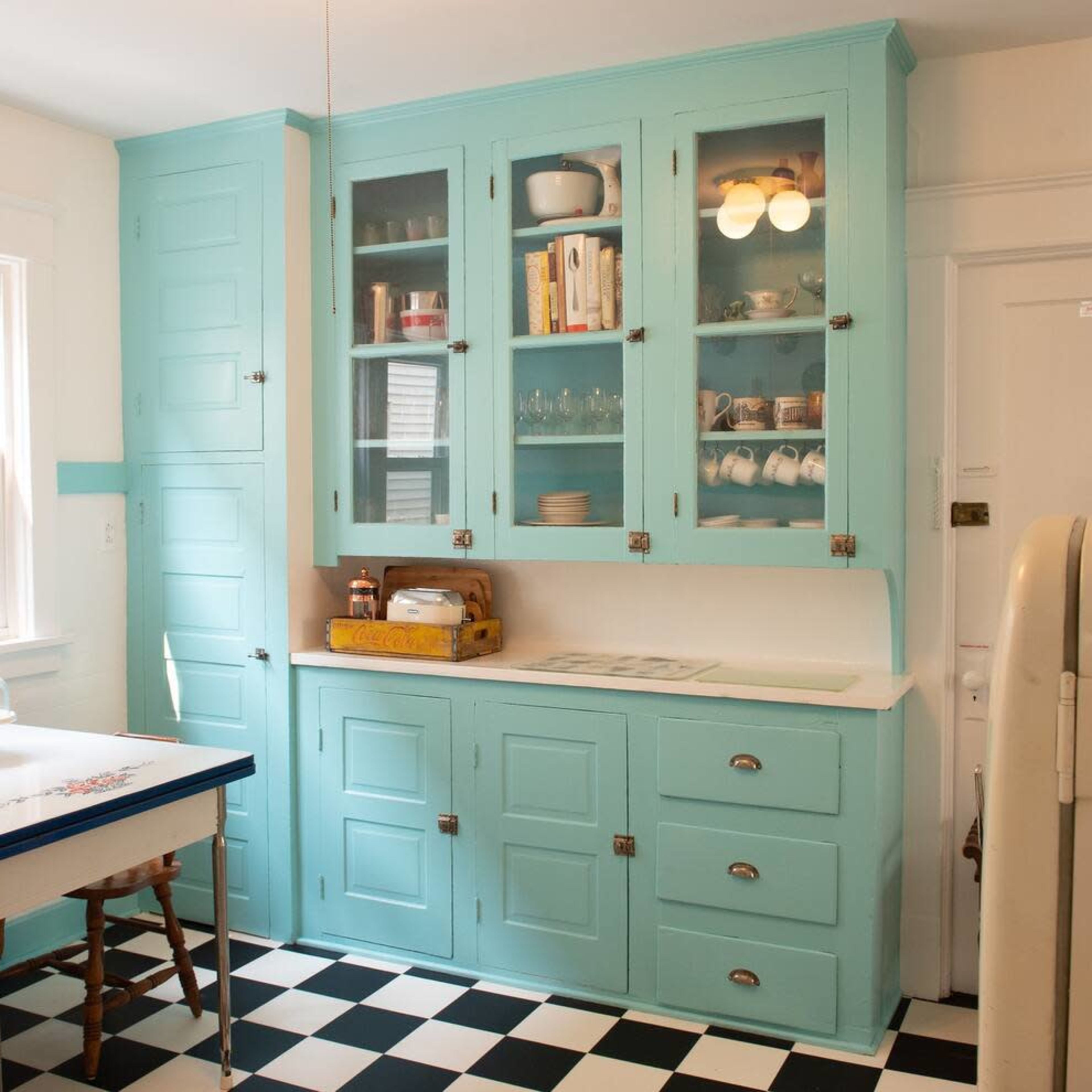 The kitchen features turquoise cabinets, a white table, and a black and white checkered floor.