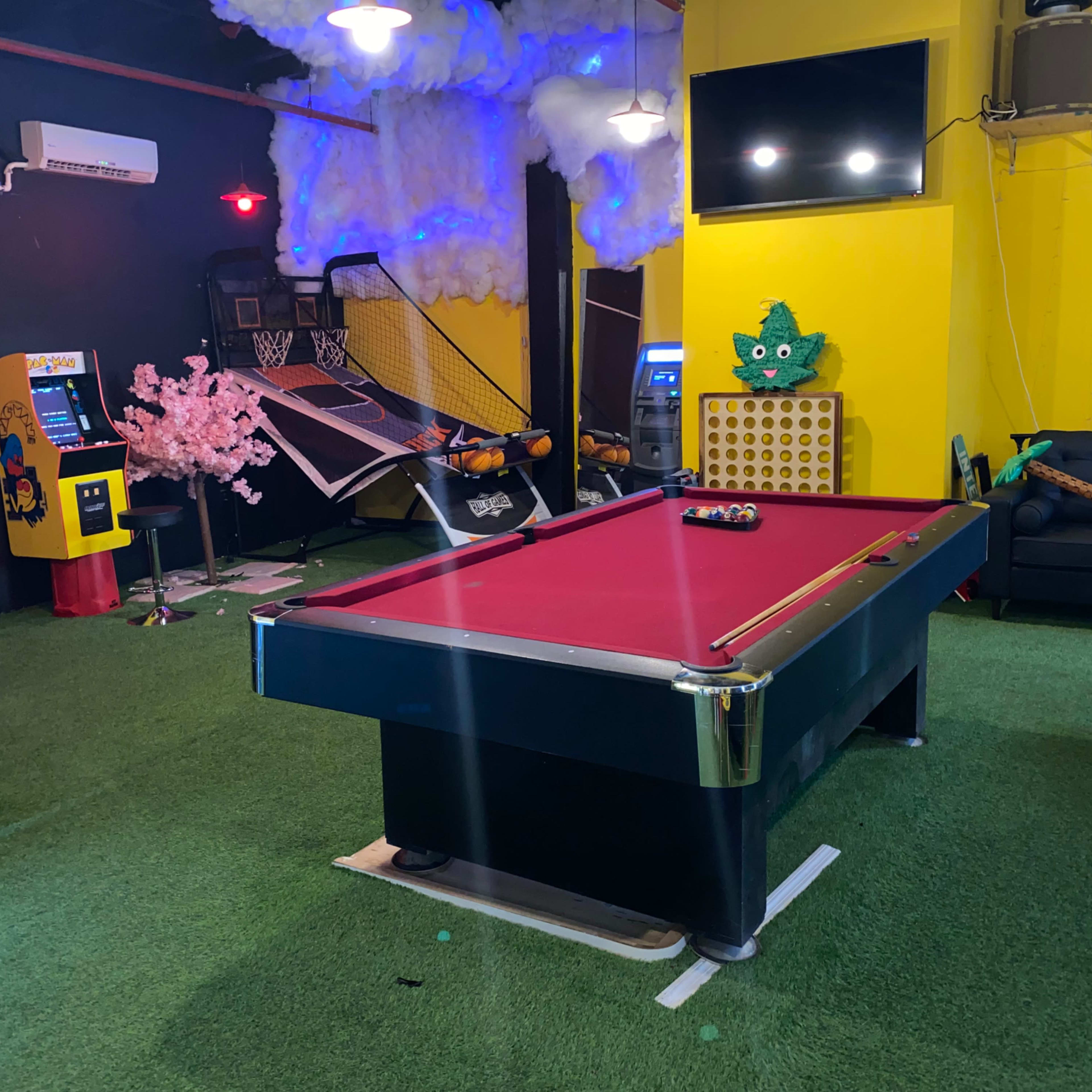 The room features a pool table at the center, surrounded by a basketball hoop, arcade game machine, and various seating and decorative elements.