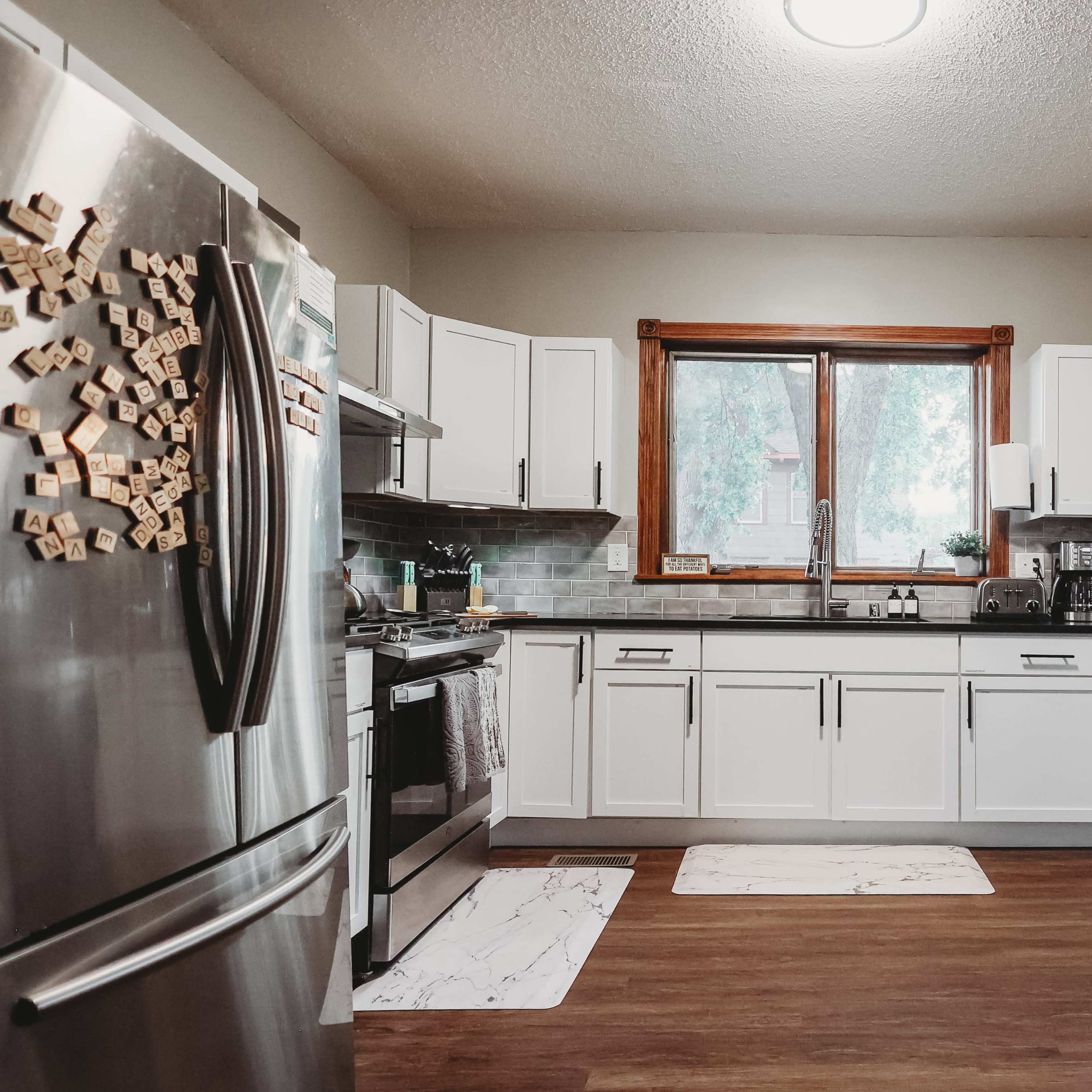 A modern kitchen features stainless steel appliances, white cabinetry, and a window overlooking a natural view.