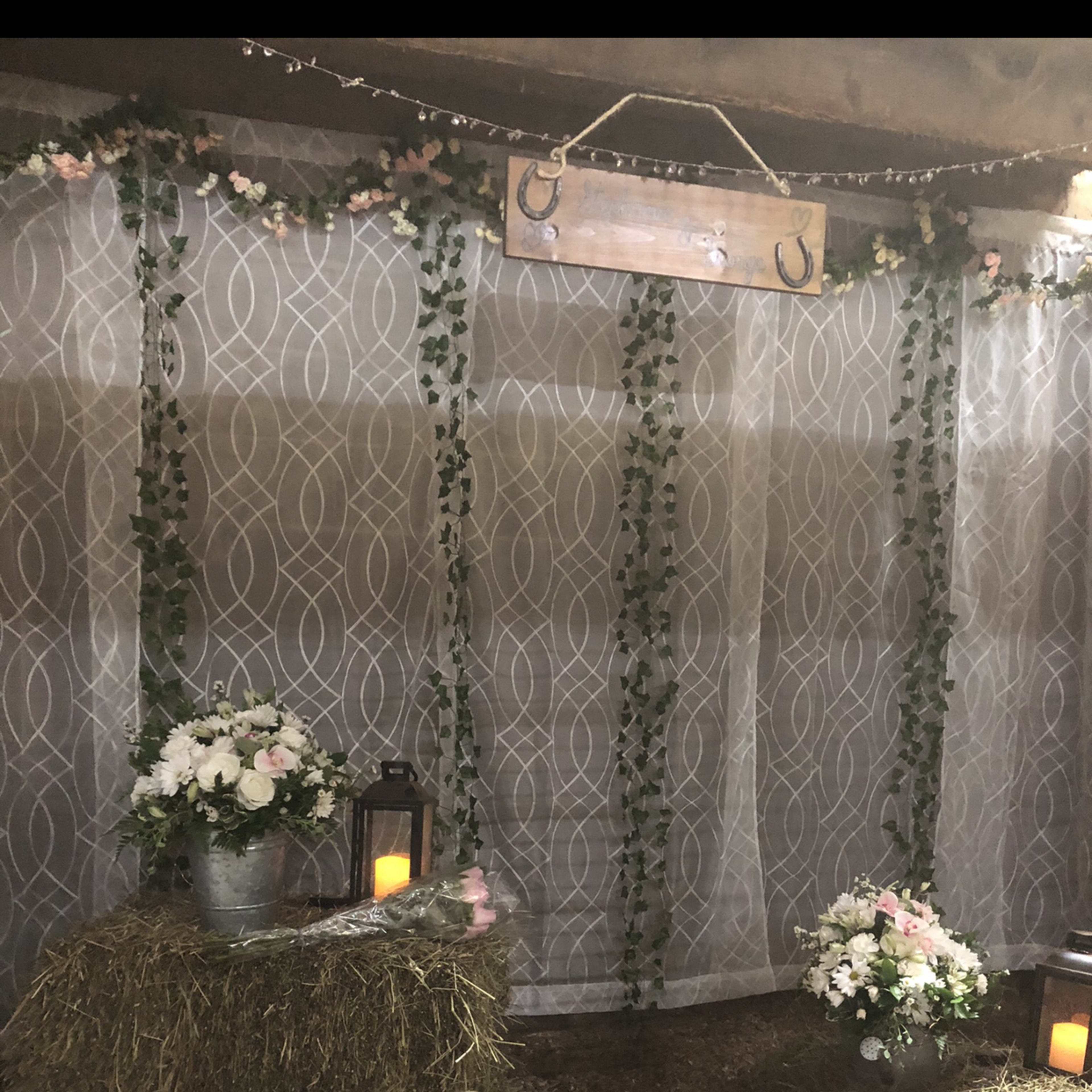 A decorated barn interior with hay bales serving as seating, floral arrangements in buckets, and lanterns on display.