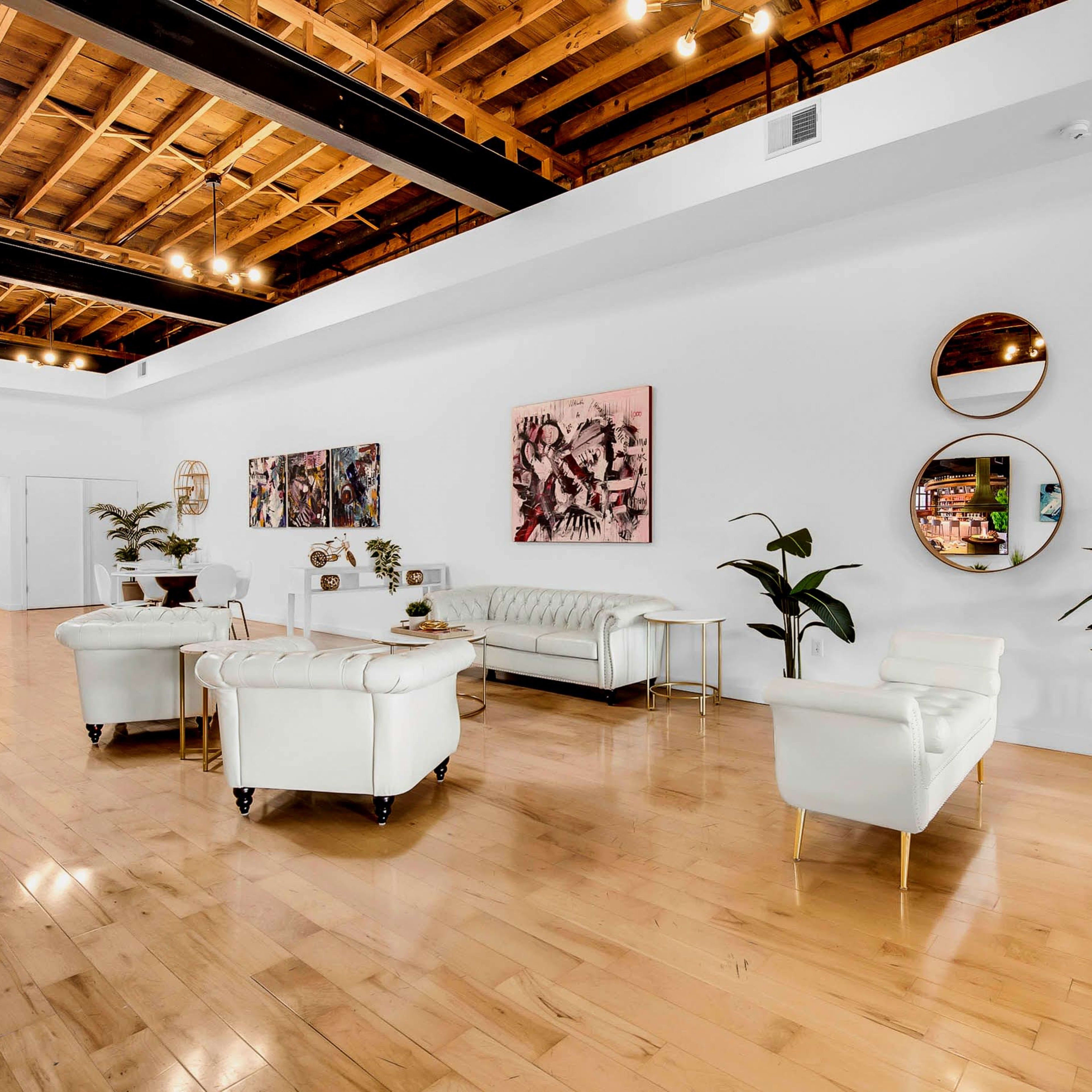 A bright, open interior space features white walls, wooden flooring, modern furnishings, and decorative art on display.