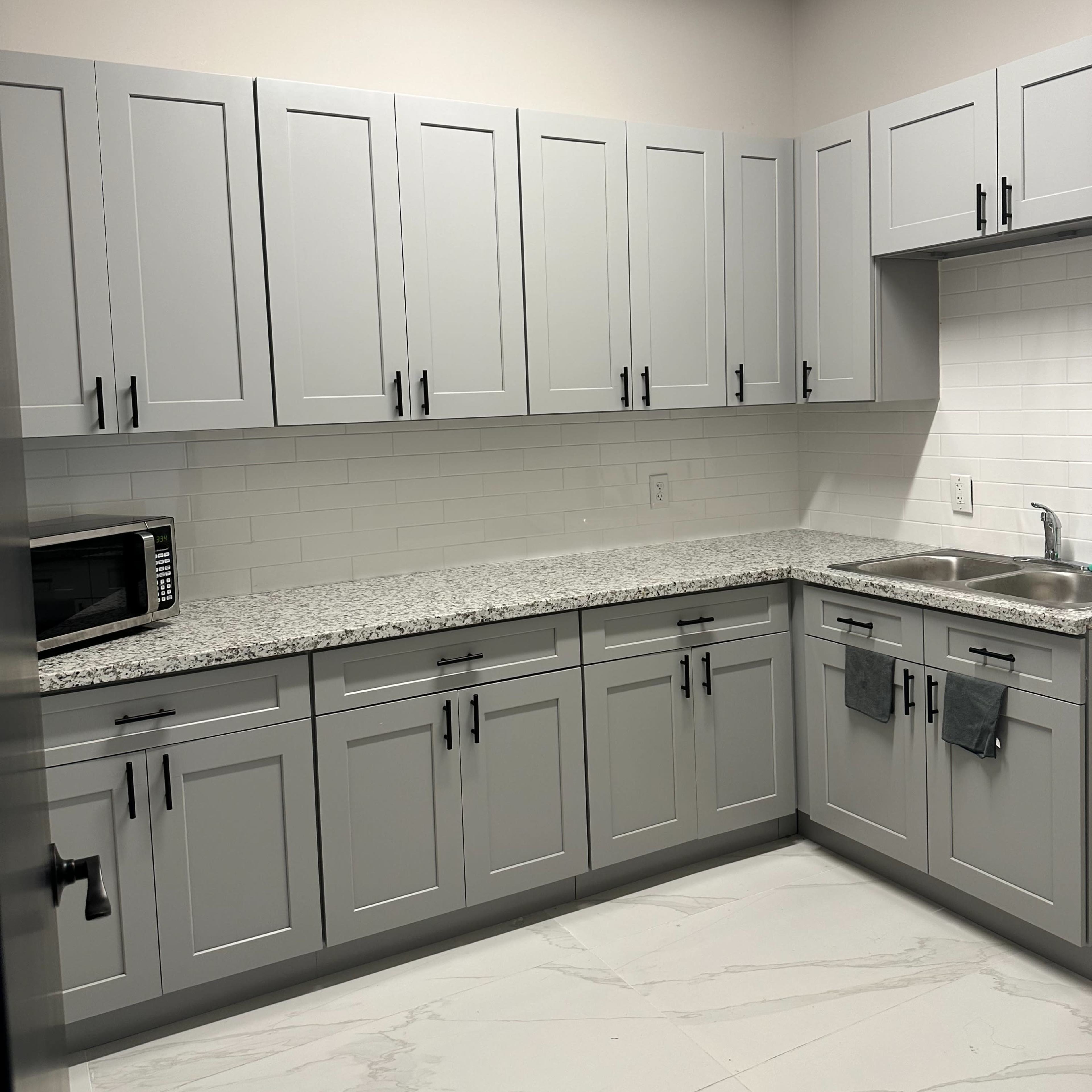 A modern kitchen with gray cabinetry, a granite countertop, and stainless steel appliances, including a microwave and sink.