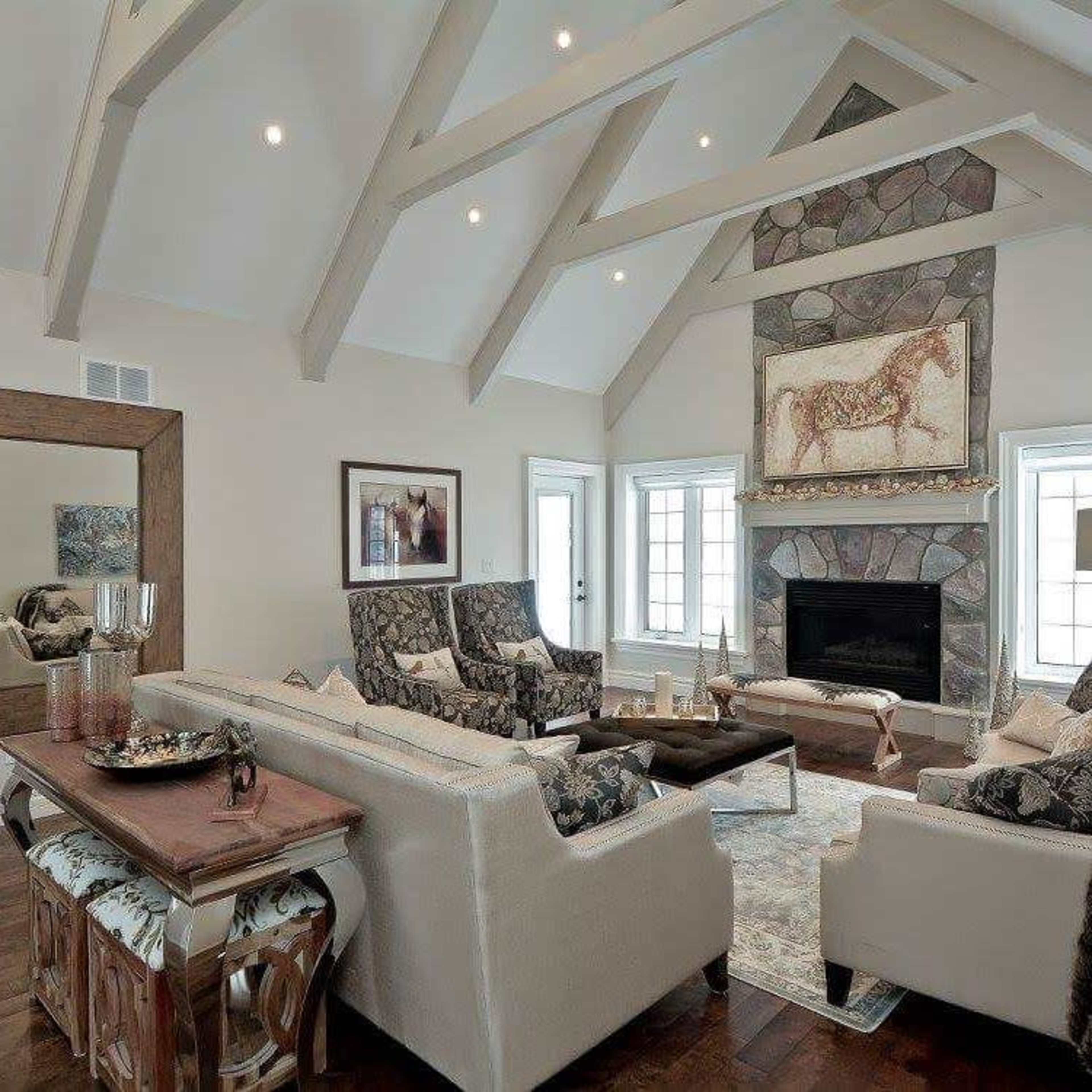 The living room features high vaulted ceilings, stone fireplace, and a mix of patterned armchairs and a neutral sofa arranged around a wooden coffee table.