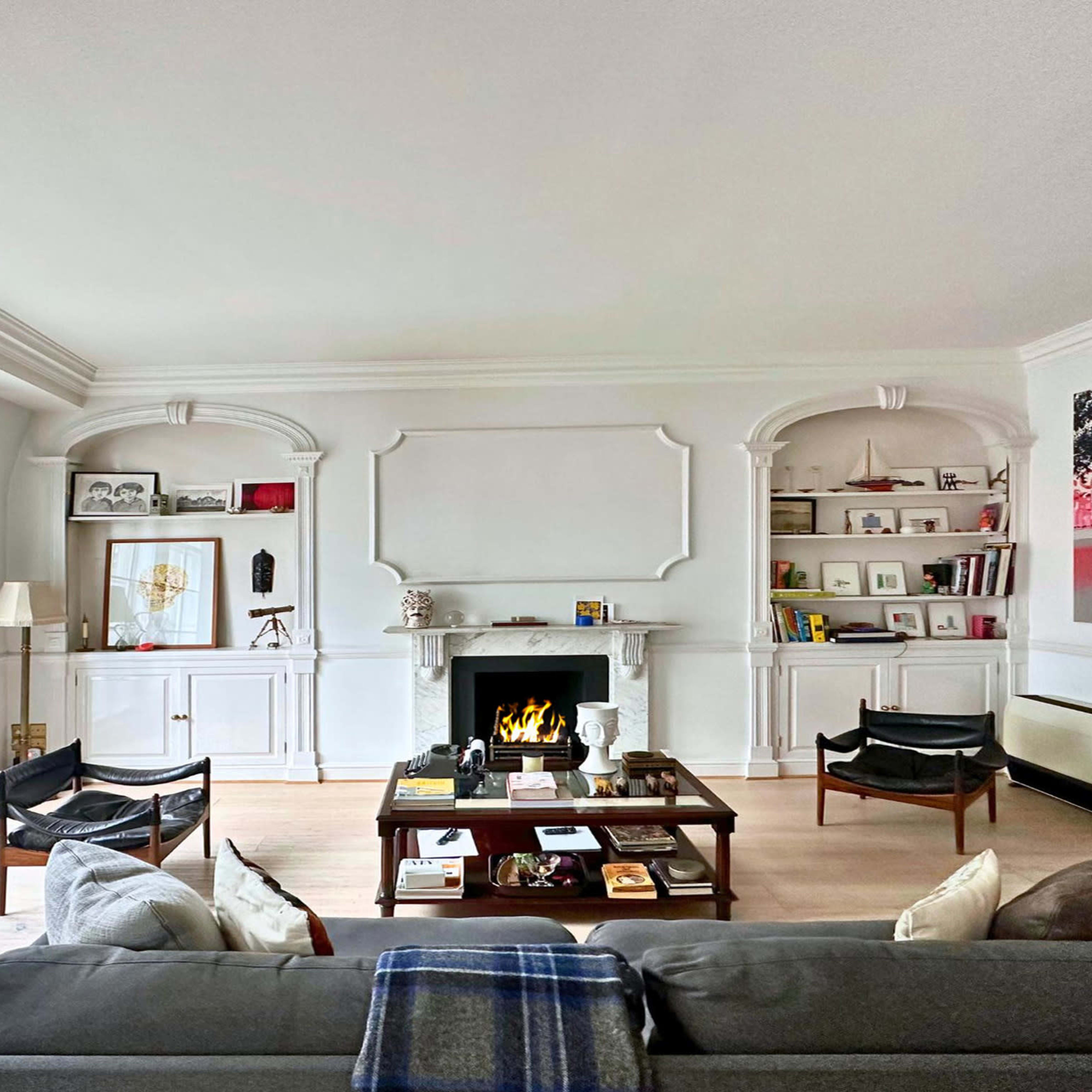 A modern living room featuring a fireplace, bookshelves, a coffee table, and large windows allowing natural light to enter.