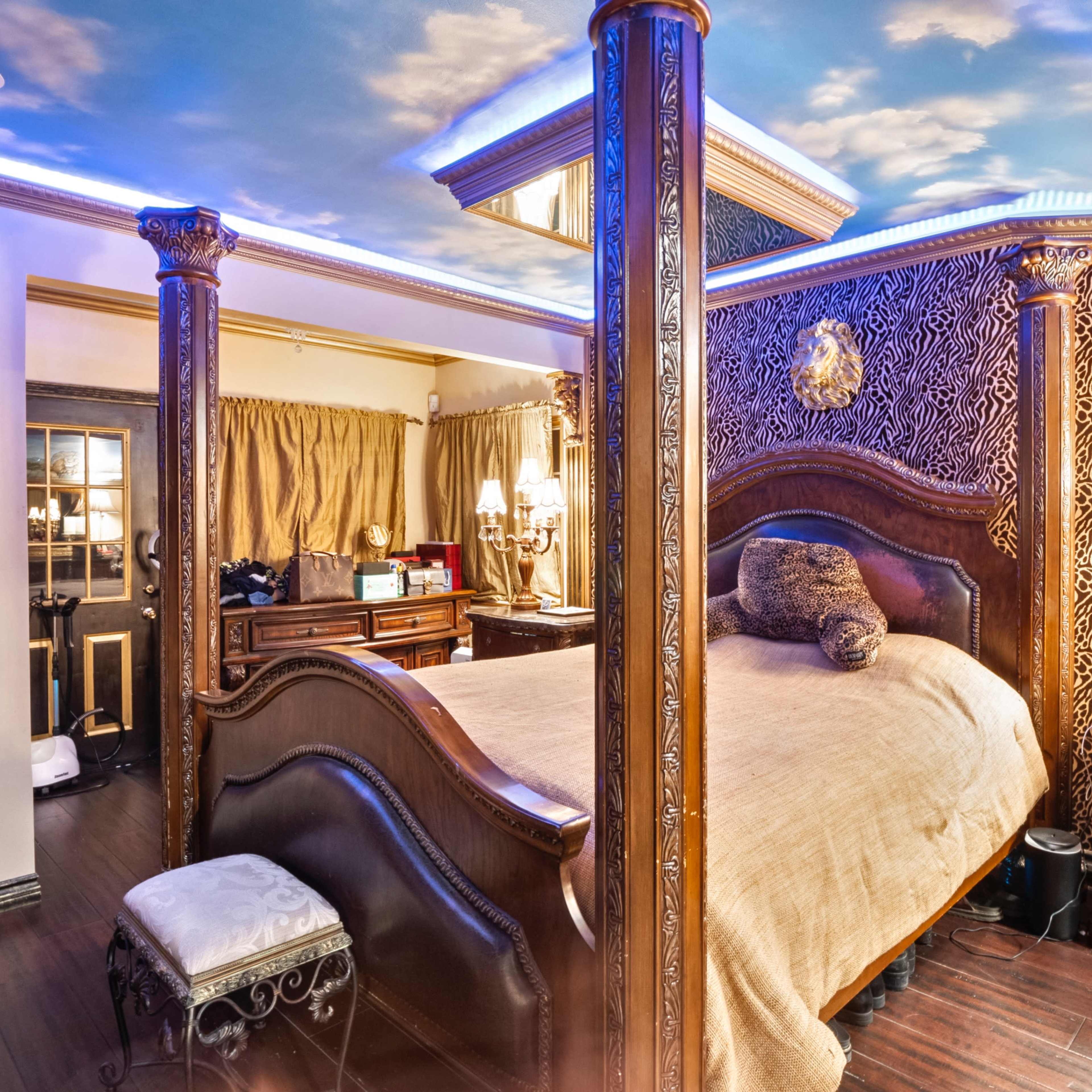 A bedroom featuring a four-poster bed with a plush blanket, decorative wall accents, elegant lighting, and polished wooden furnishings.
