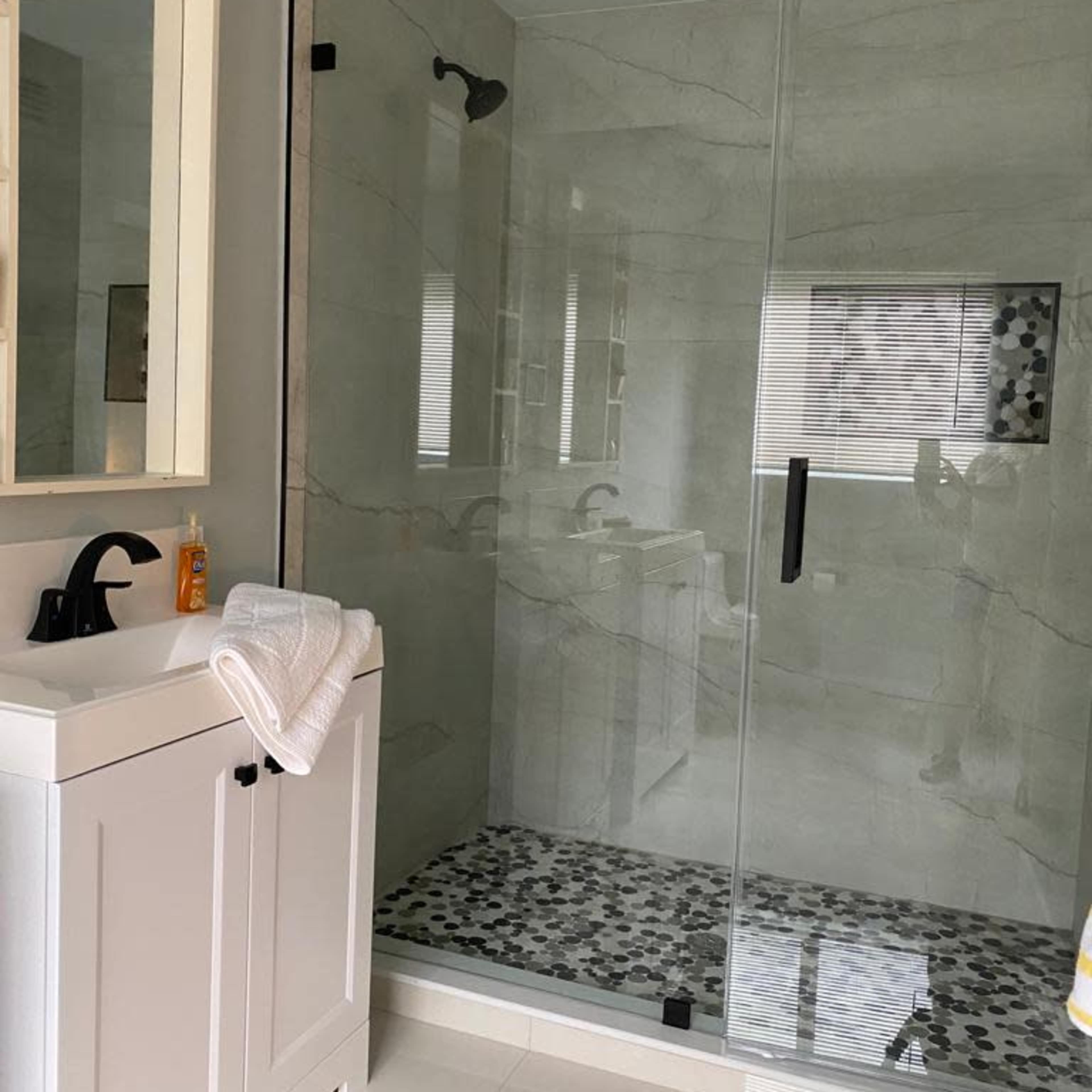 A modern bathroom featuring a glass-enclosed shower, a white vanity, and a tiled floor with black and white patterns.