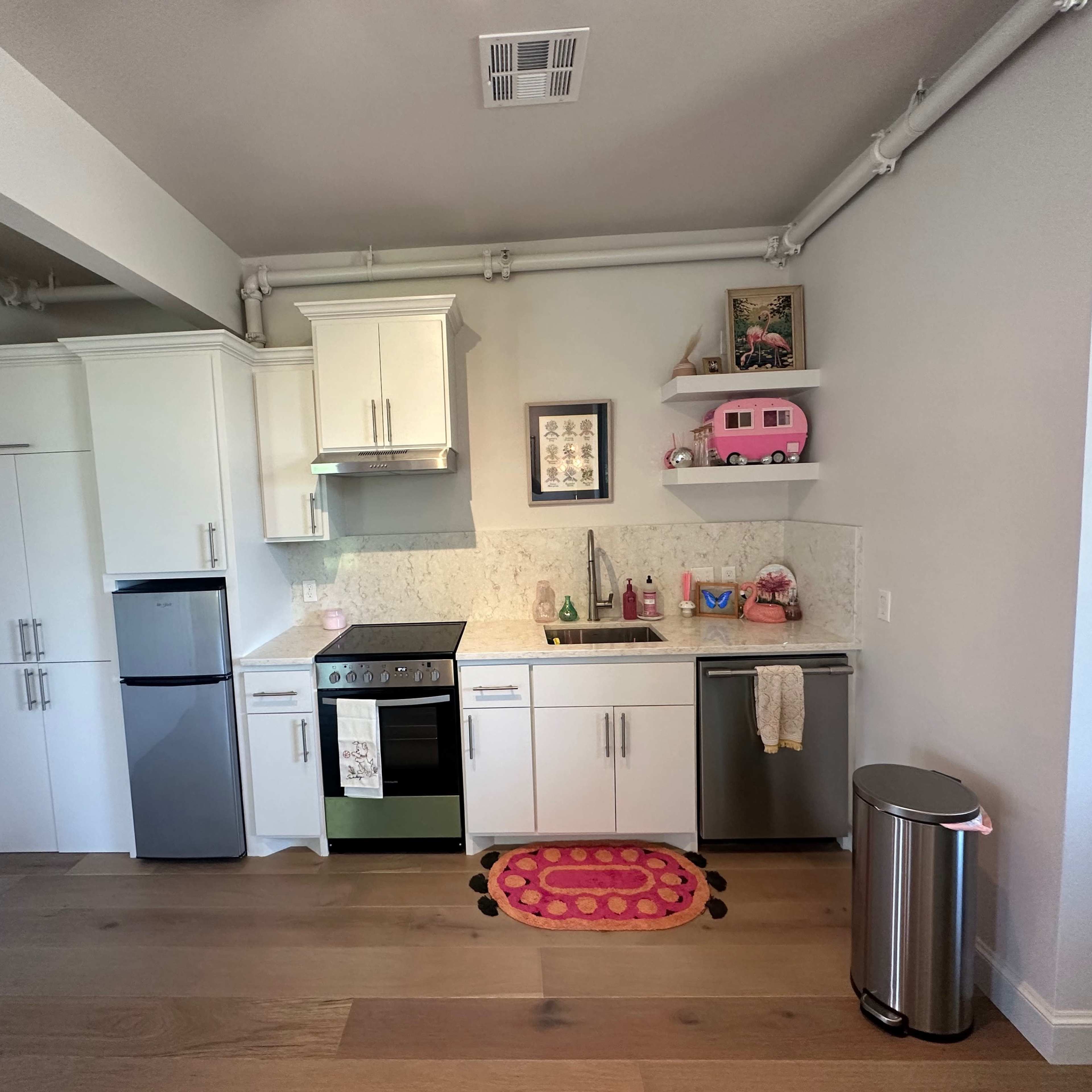 A modern kitchen layout with white cabinets, a stainless steel refrigerator, a stove, and decorative items on the shelves.