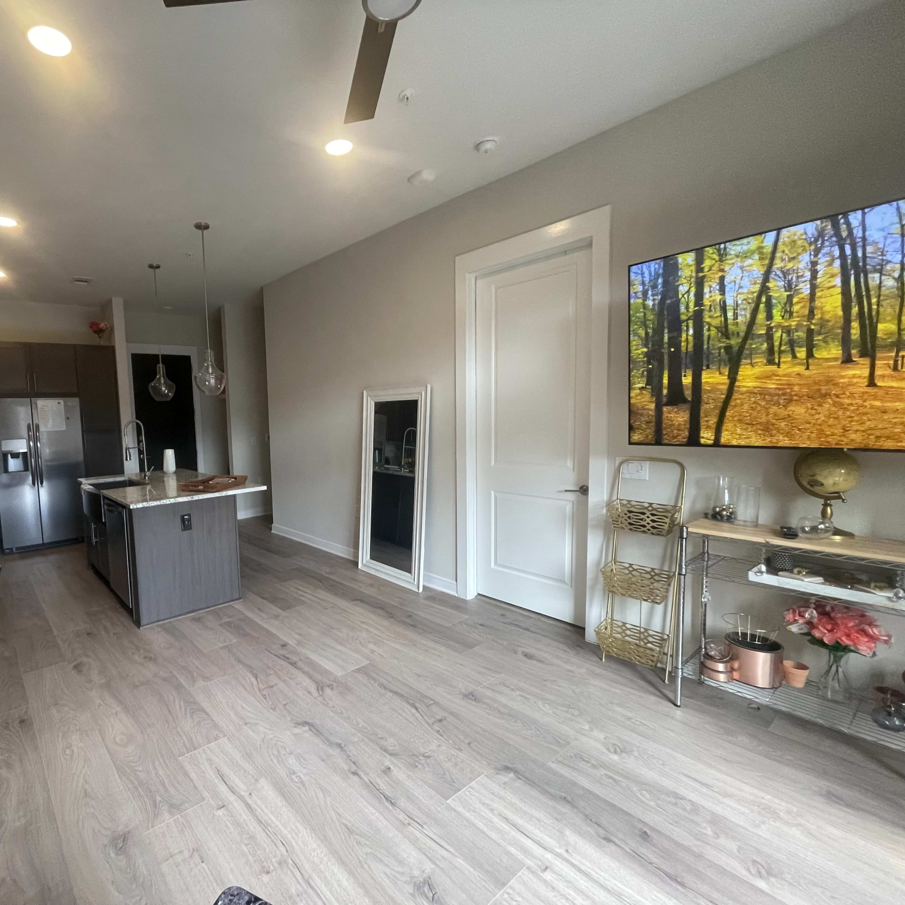 A modern kitchen and living area with gray cabinetry, a central island, and a large wall-mounted television displaying a nature scene.