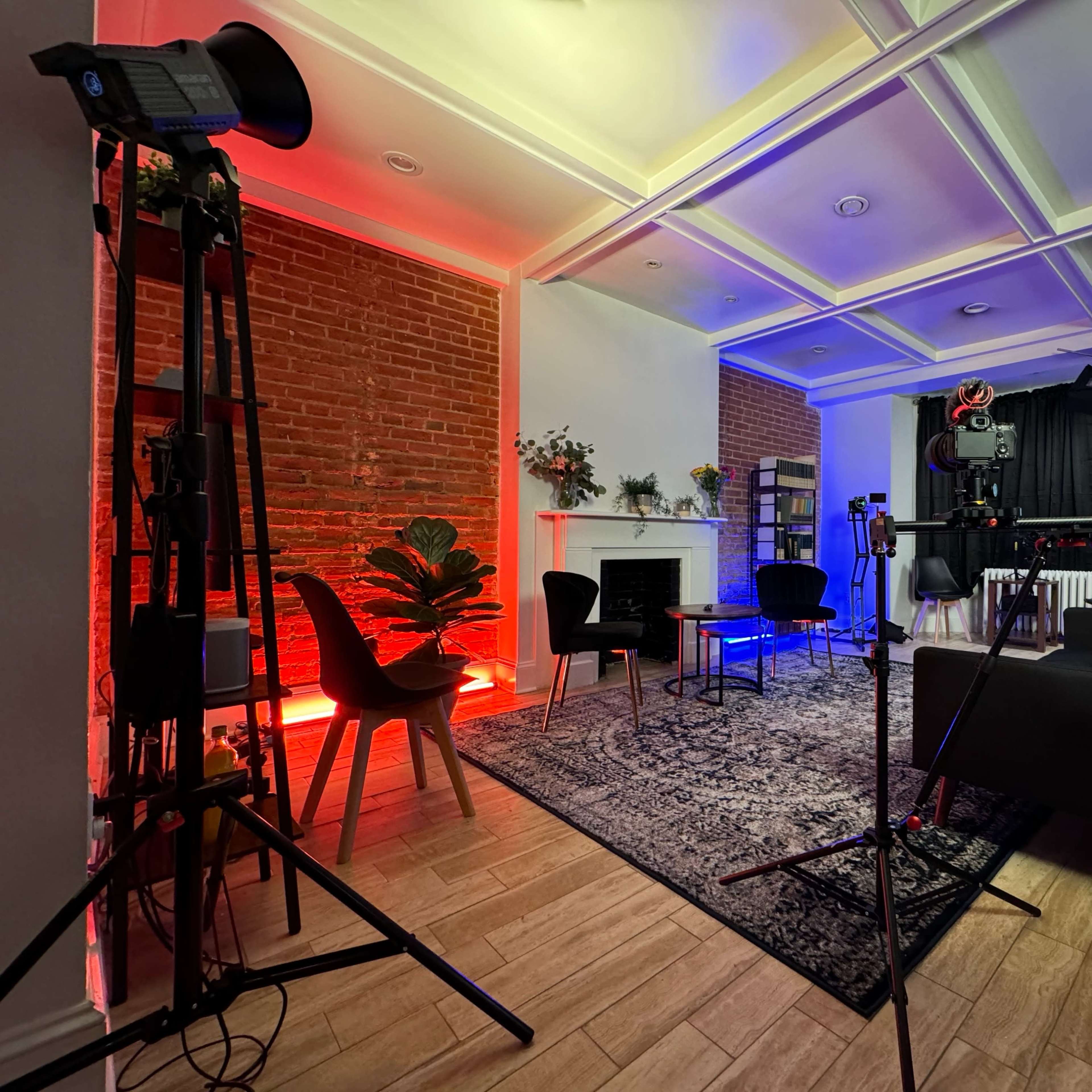 A modern studio setup featuring a seating area, lighting equipment, and a backdrop against a brick wall.