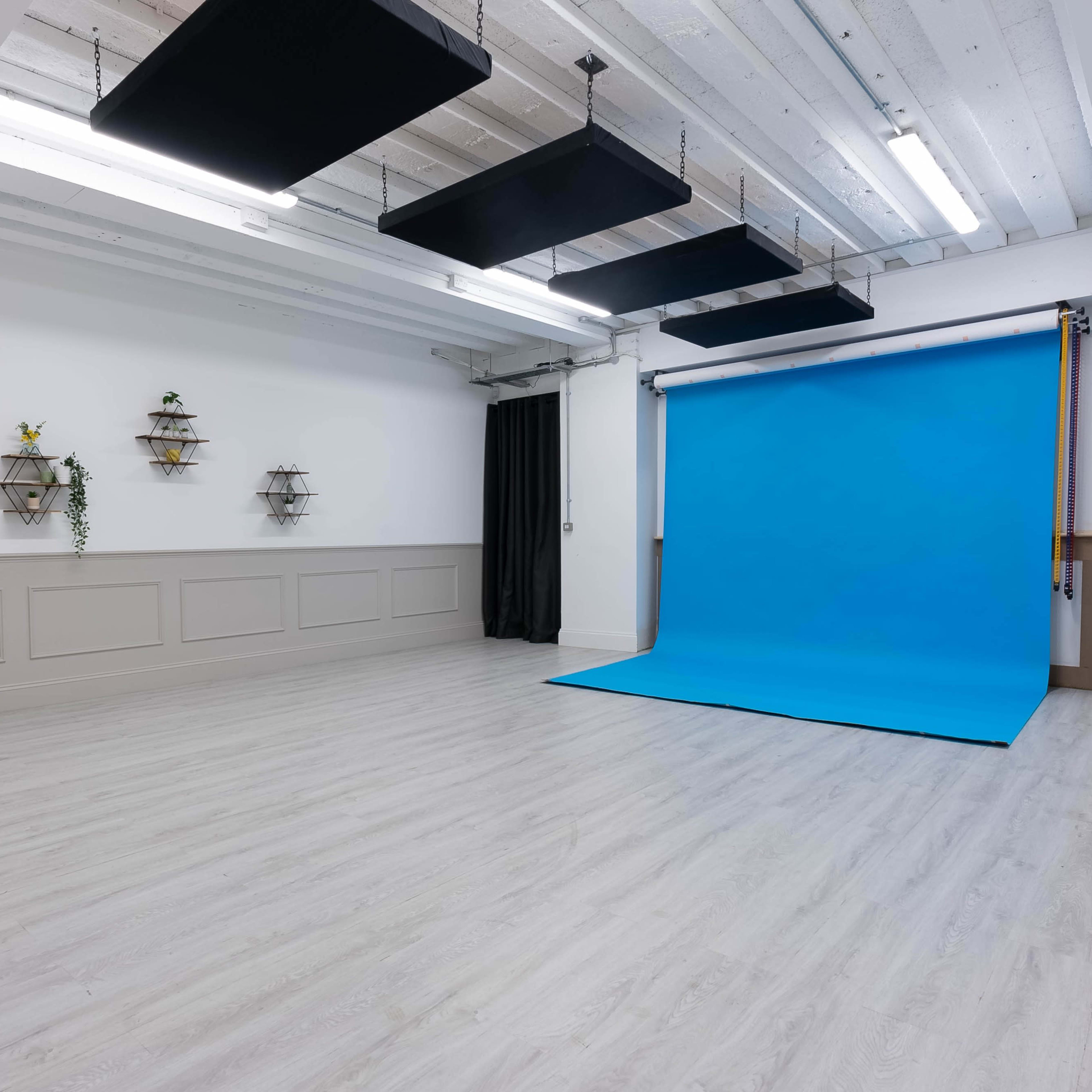 A spacious, empty studio featuring a bright blue backdrop and wooden floors, with shelves on the walls.
