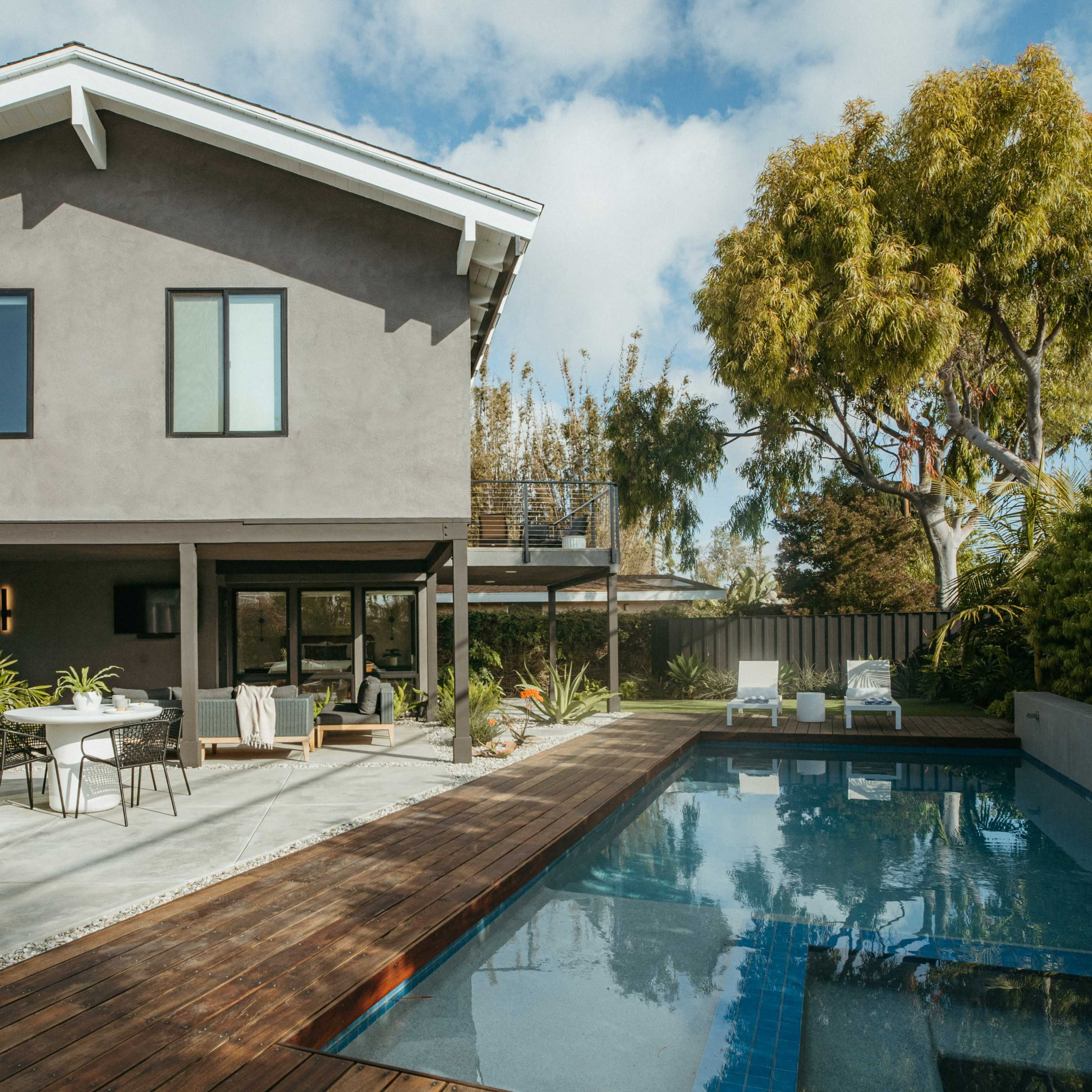 A modern house with a gray exterior features an outdoor patio, a swimming pool, and landscaped greenery.
