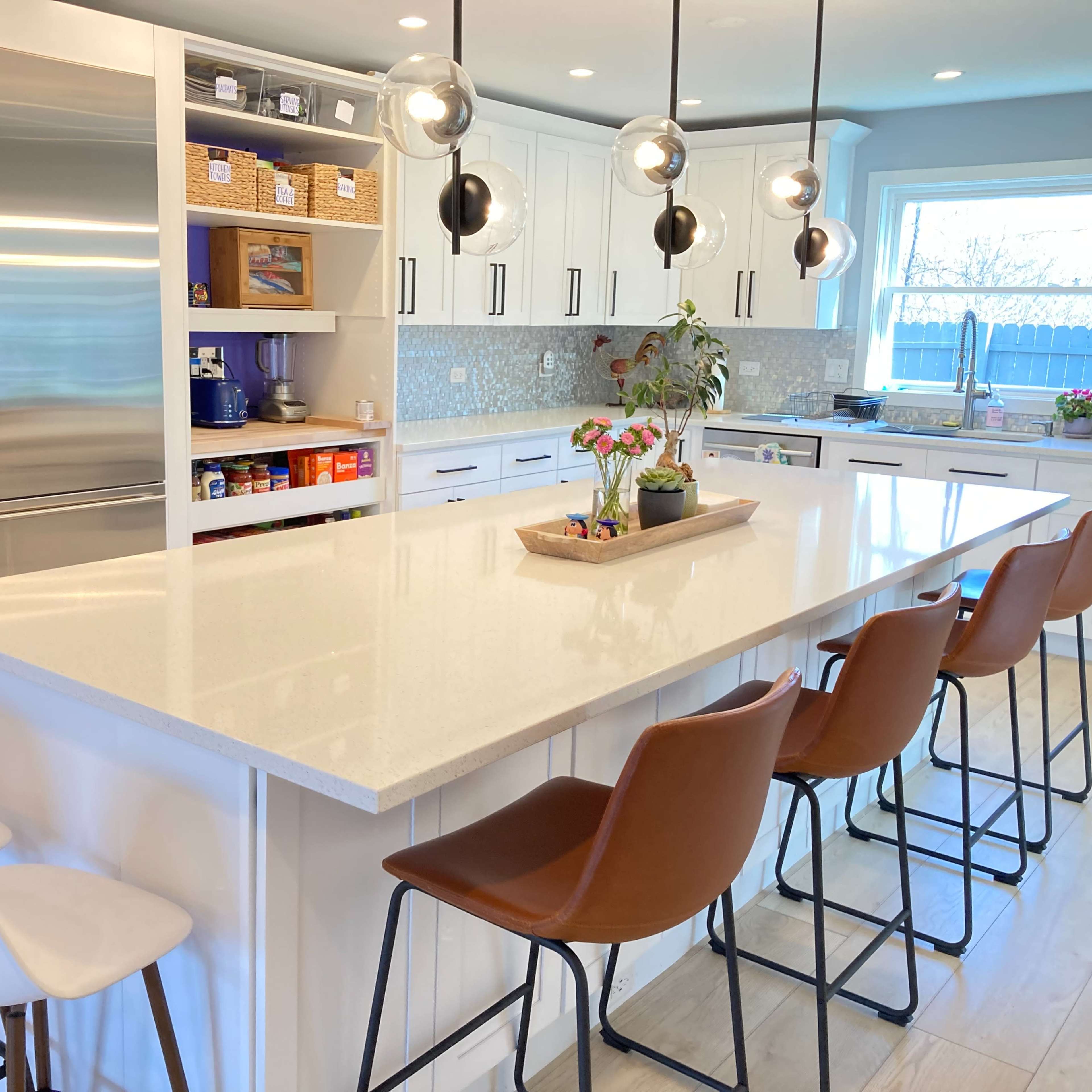 A modern kitchen featuring a large island with bar stools, stainless steel appliances, and white cabinetry.