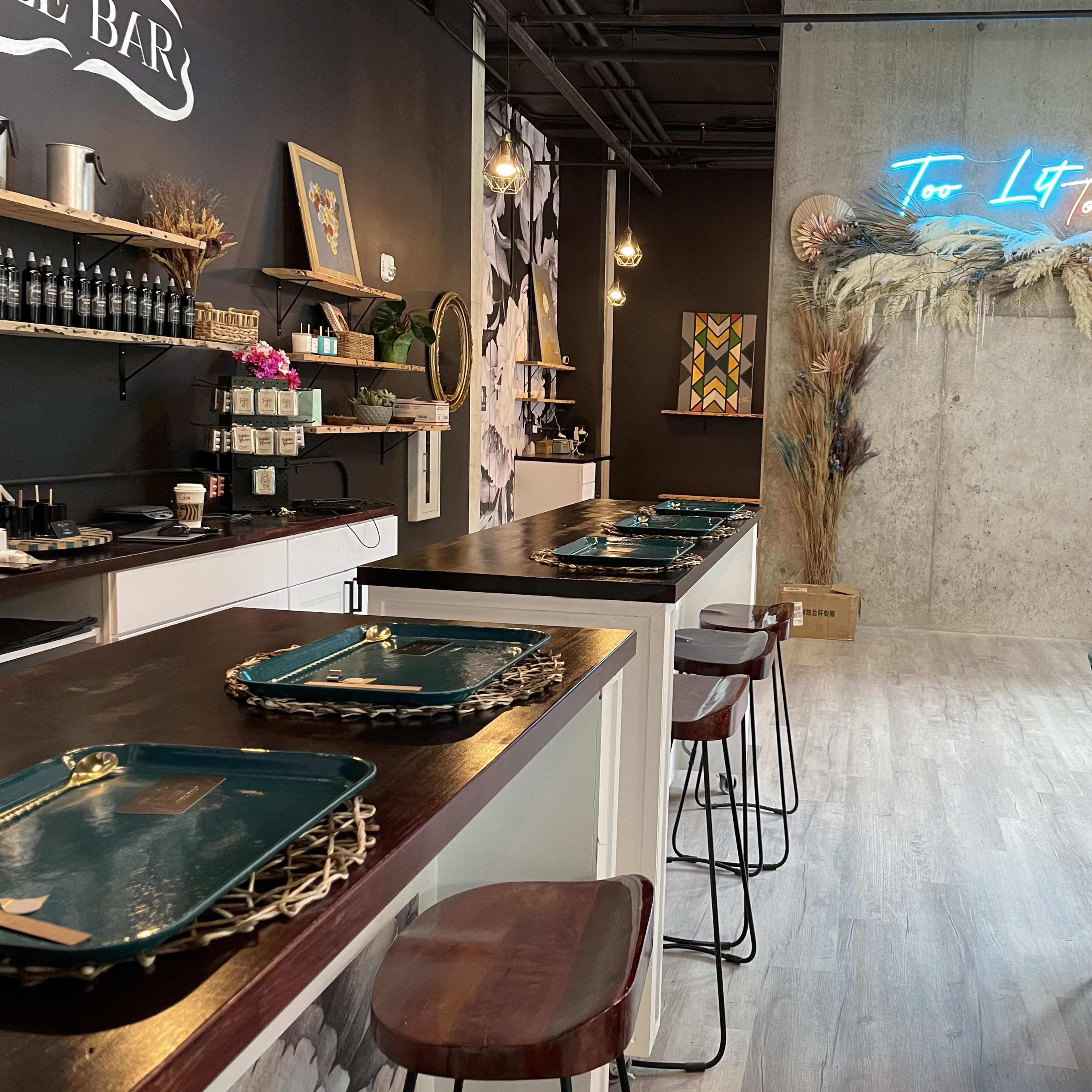 A modern café interior with wooden tables, teal chairs, and a neon sign against a concrete wall.