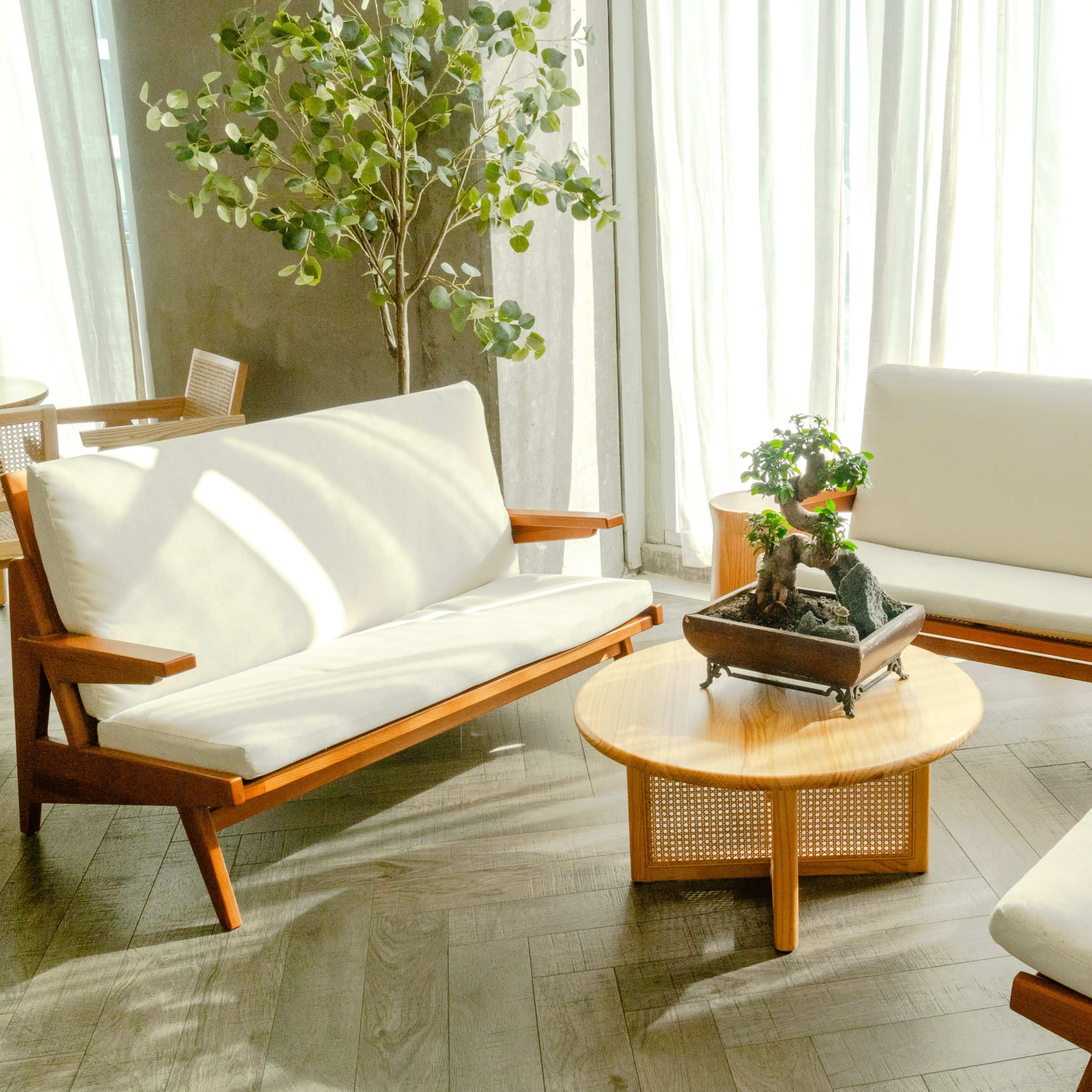 A modern seating area with two white couches and a wooden coffee table, surrounded by large windows and a potted plant.