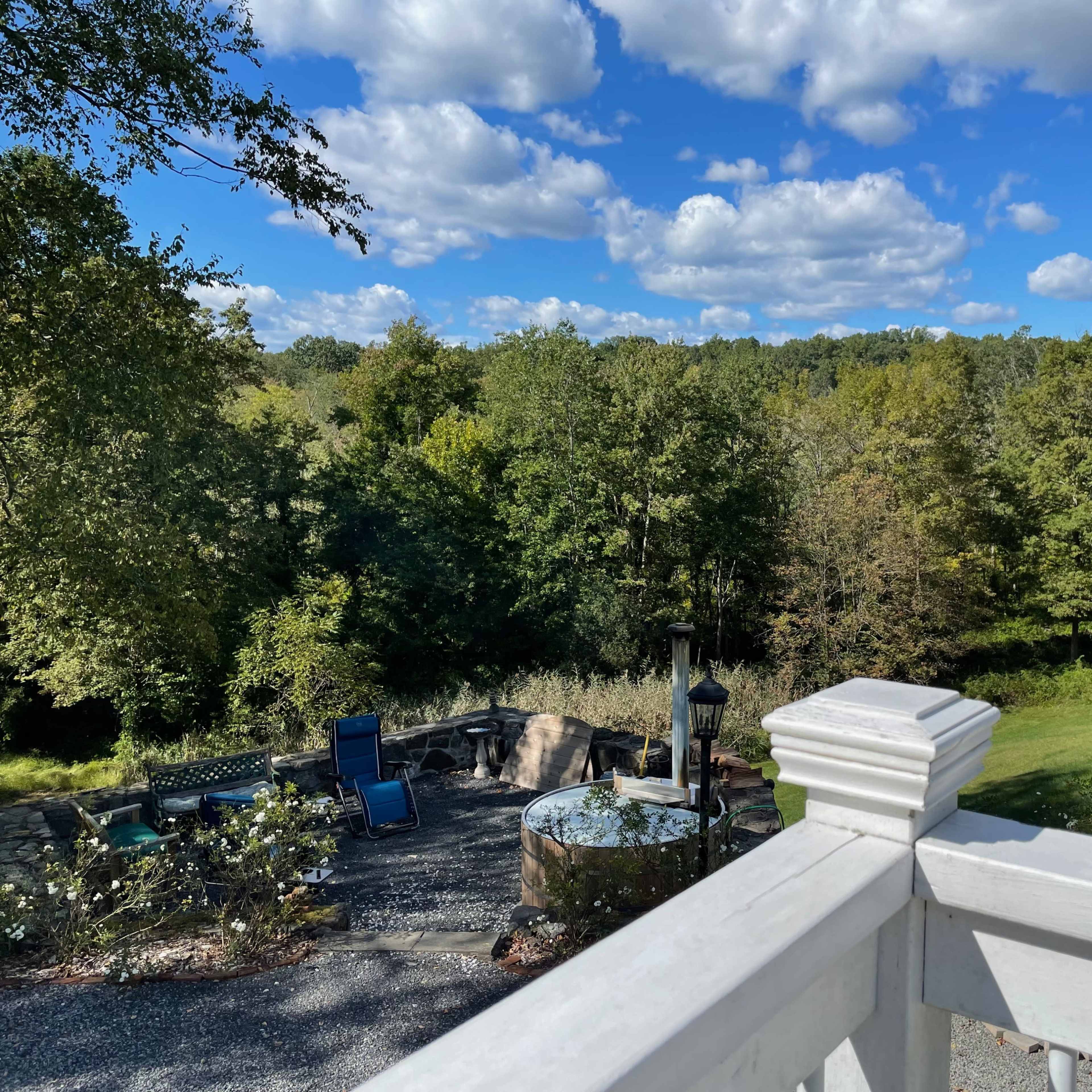 A view from a white railing overlooks a landscaped backyard with seating areas and trees under a partly cloudy sky.