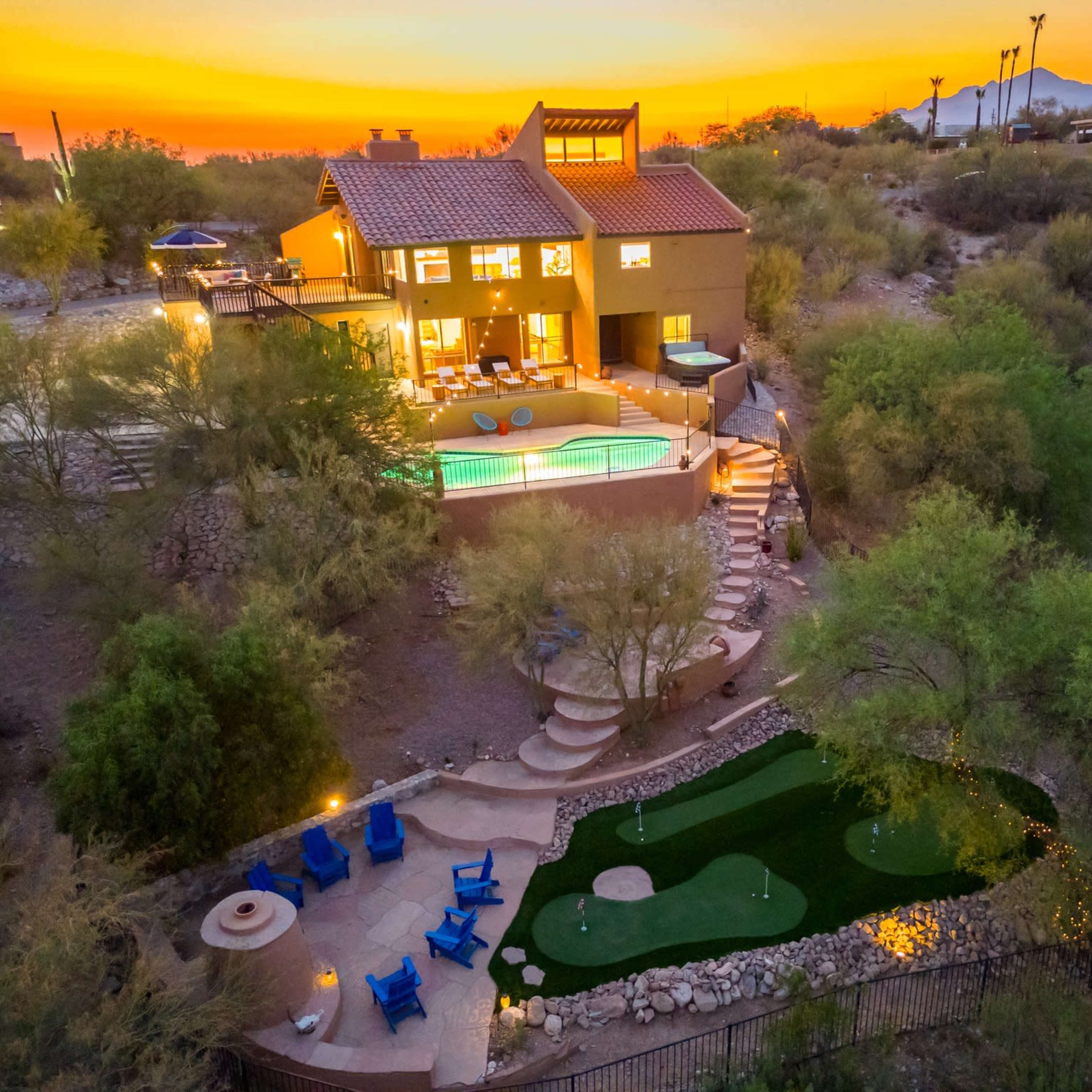 A hillside home with a swimming pool and a putting green surrounded by desert vegetation at sunset.