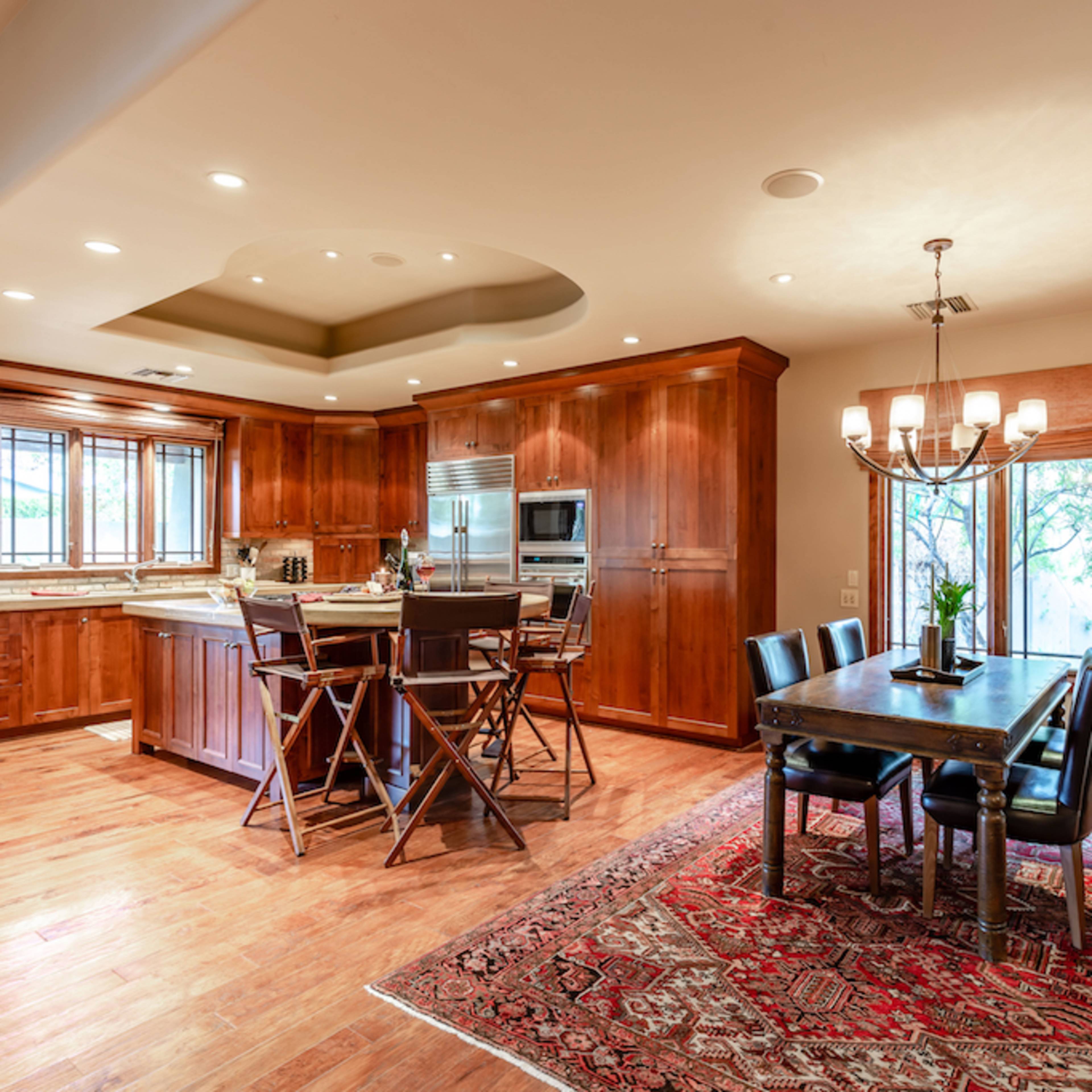 A spacious kitchen and dining area features wooden cabinetry, a large island, and a rectangular dining table with black chairs on a patterned rug.