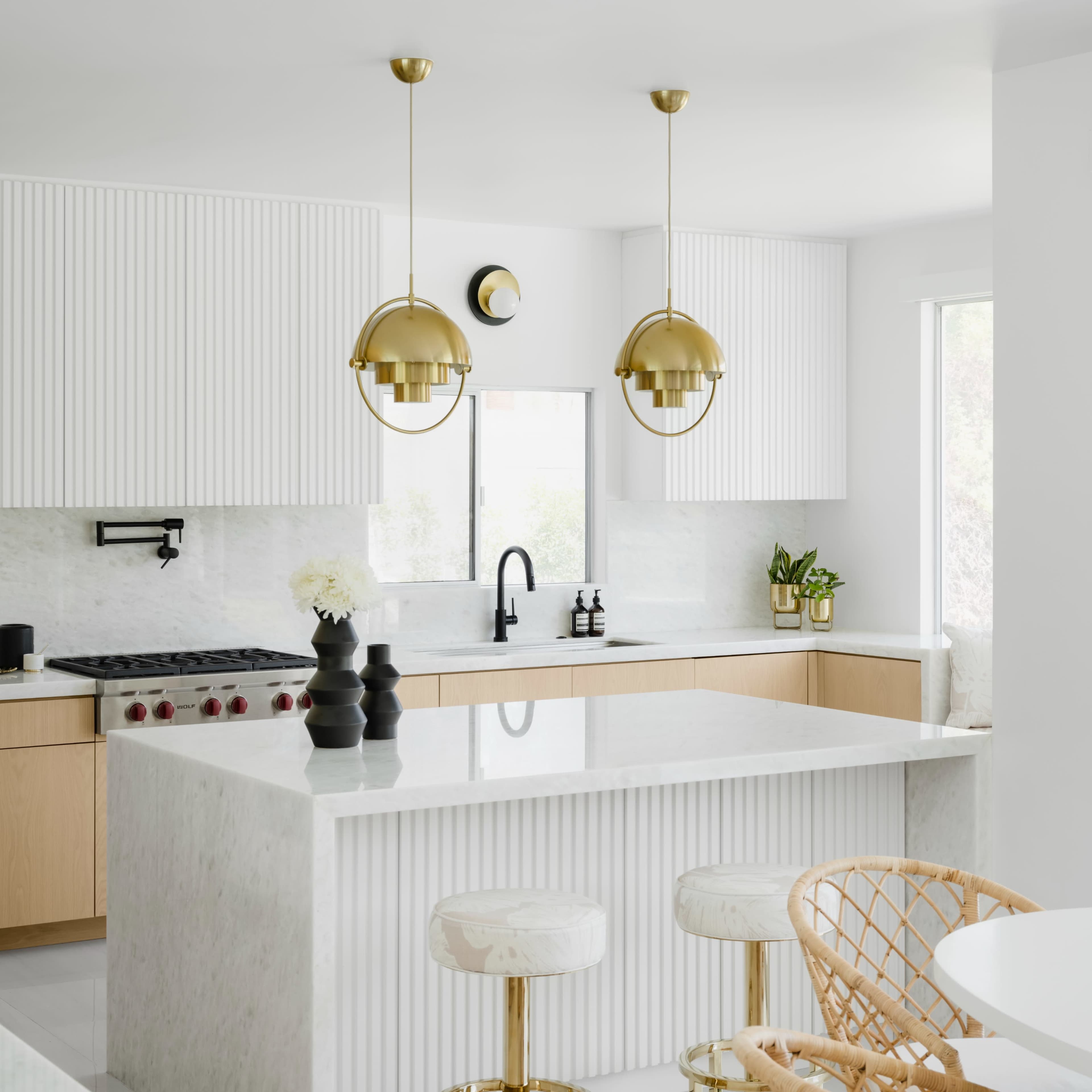 The kitchen features a marble island with gold accents, light wooden cabinetry, and modern pendant lighting.