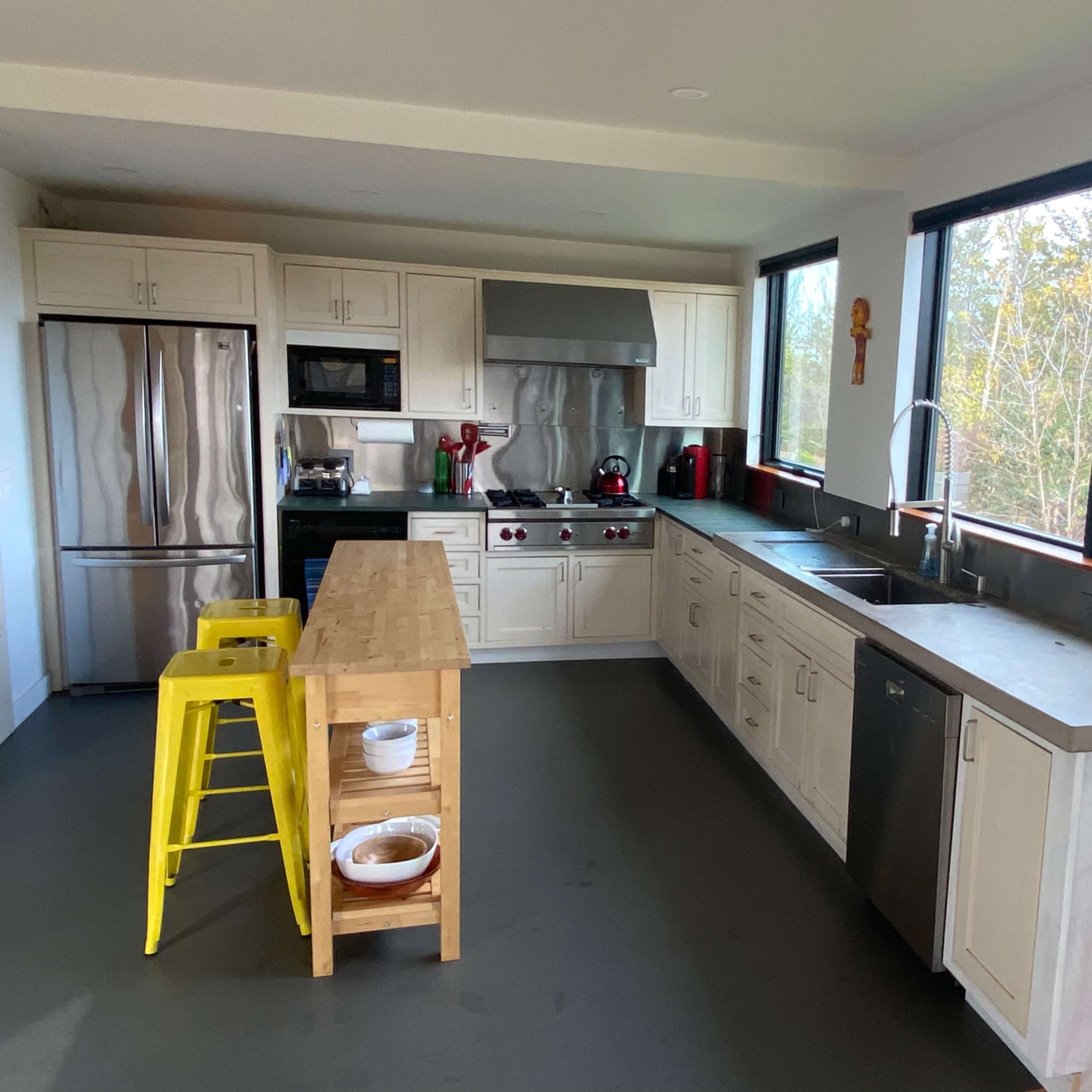 A modern kitchen with stainless steel appliances, a central wooden island, and large windows facing a view of trees.
