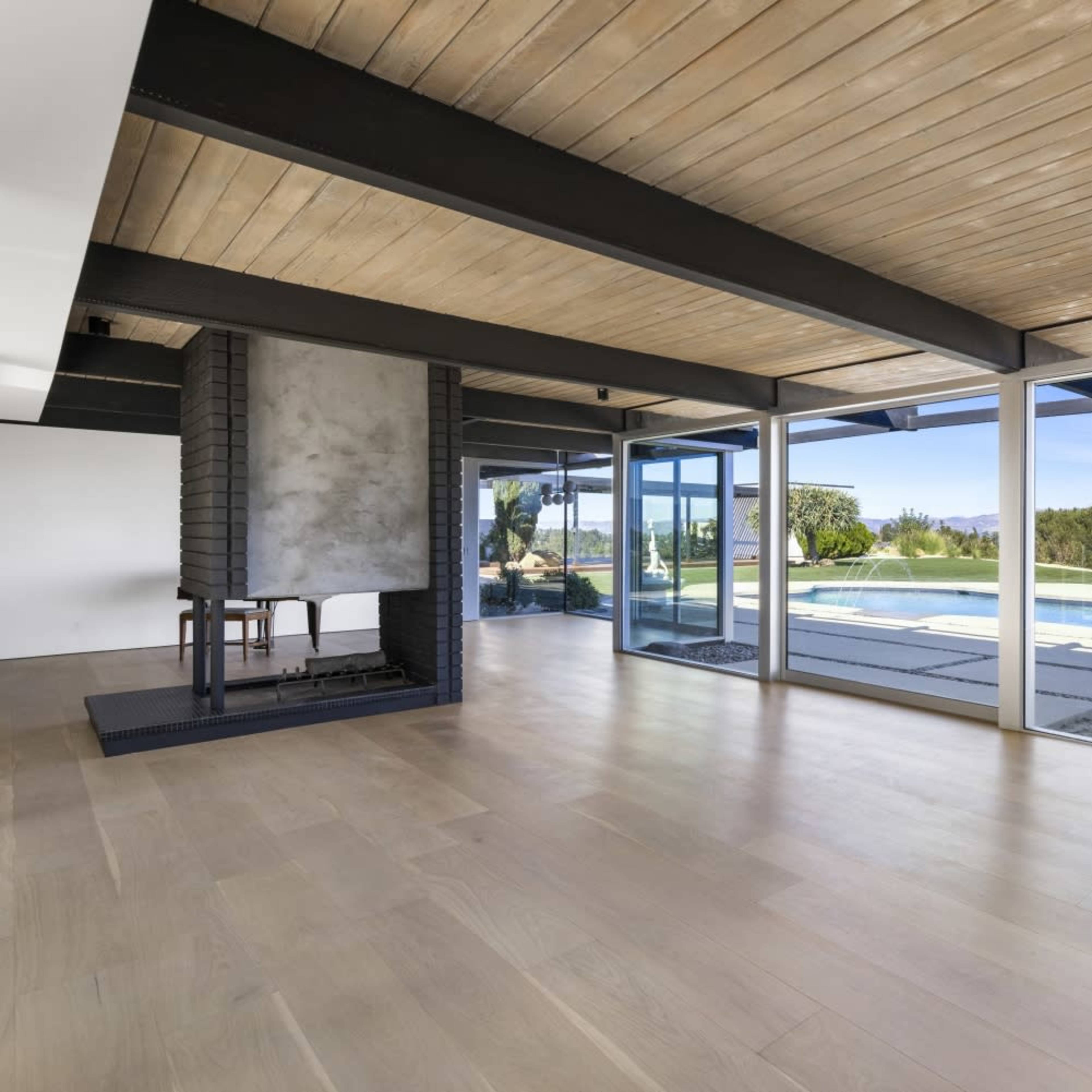 The interior space features large windows overlooking a pool area and a modern fireplace in a minimalist setting.