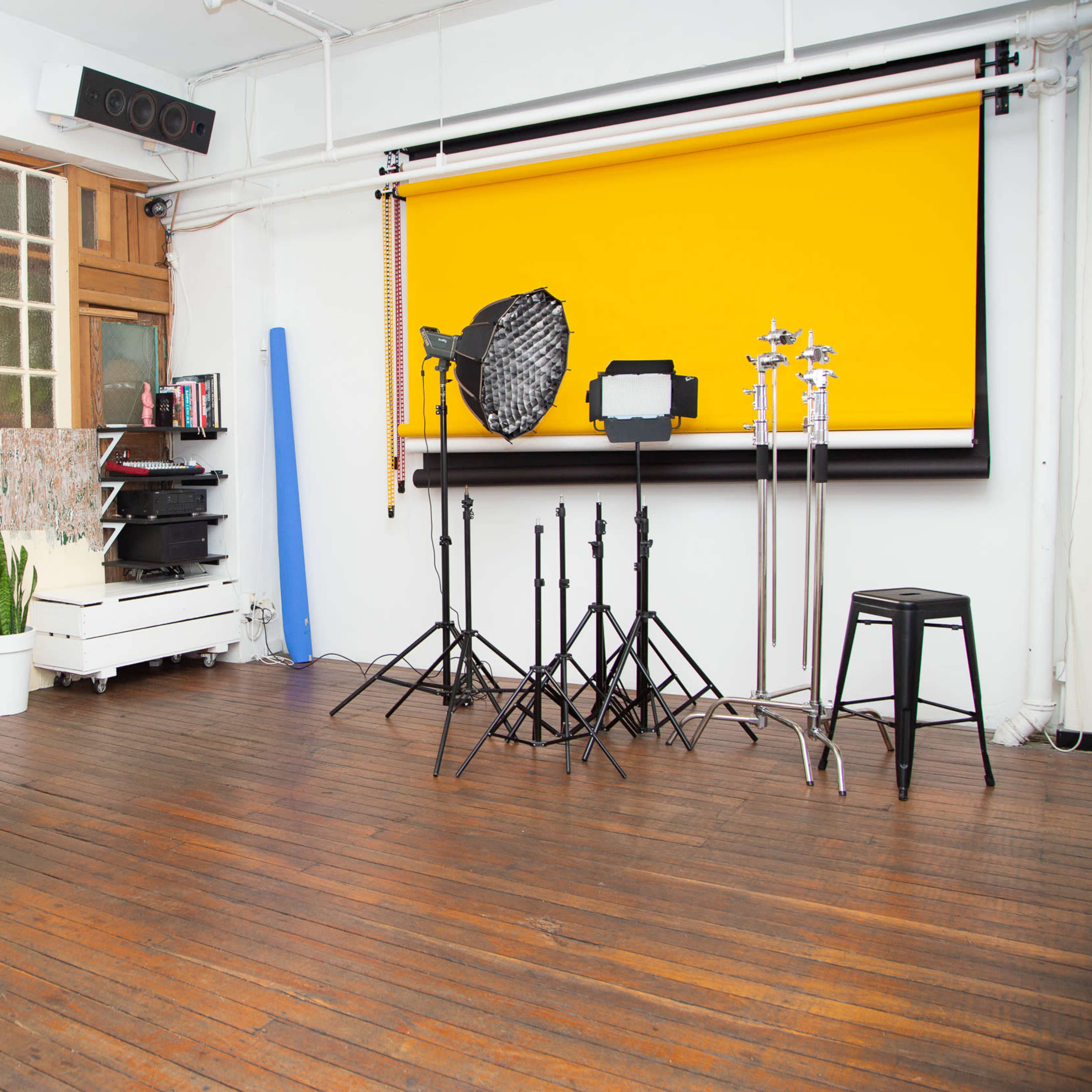 A photography studio with wooden floors, a yellow backdrop, and various lighting equipment set up on stands.