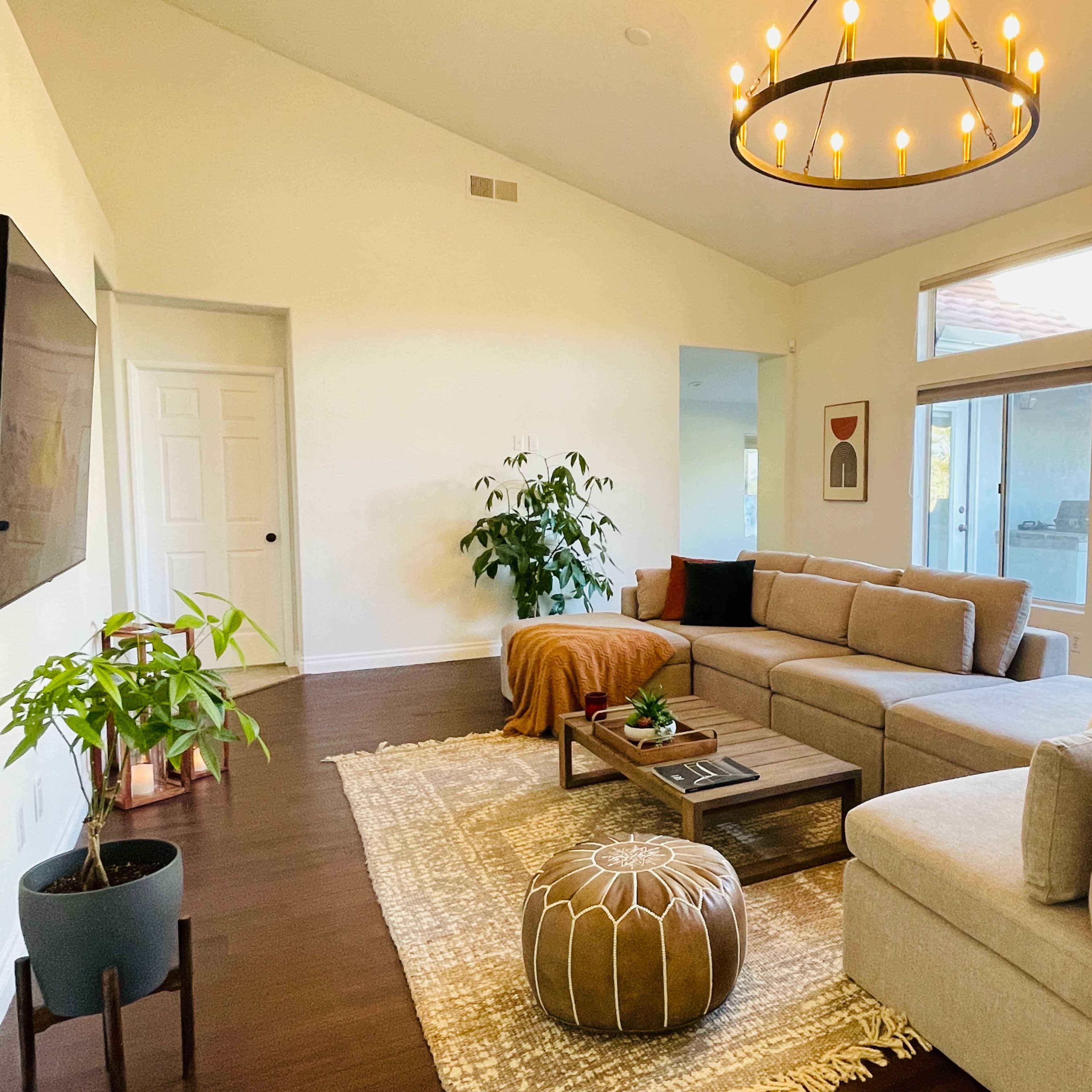 A modern living room featuring a sectional sofa, a coffee table on a patterned rug, and large windows allowing natural light to enter the space.
