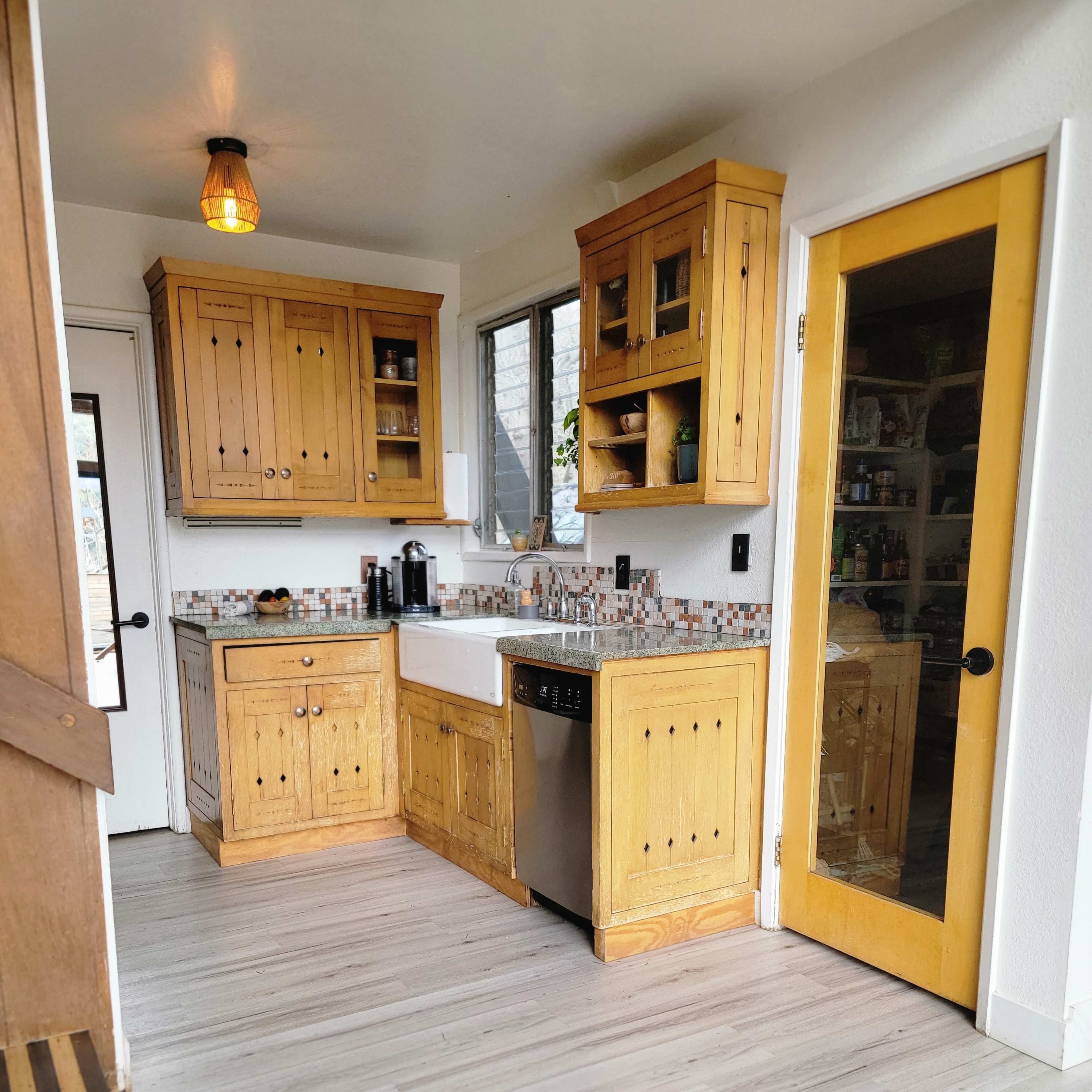 A kitchen with wooden cabinets, a sink, and a dishwasher, featuring light-colored flooring and an abundance of natural light from a nearby window.