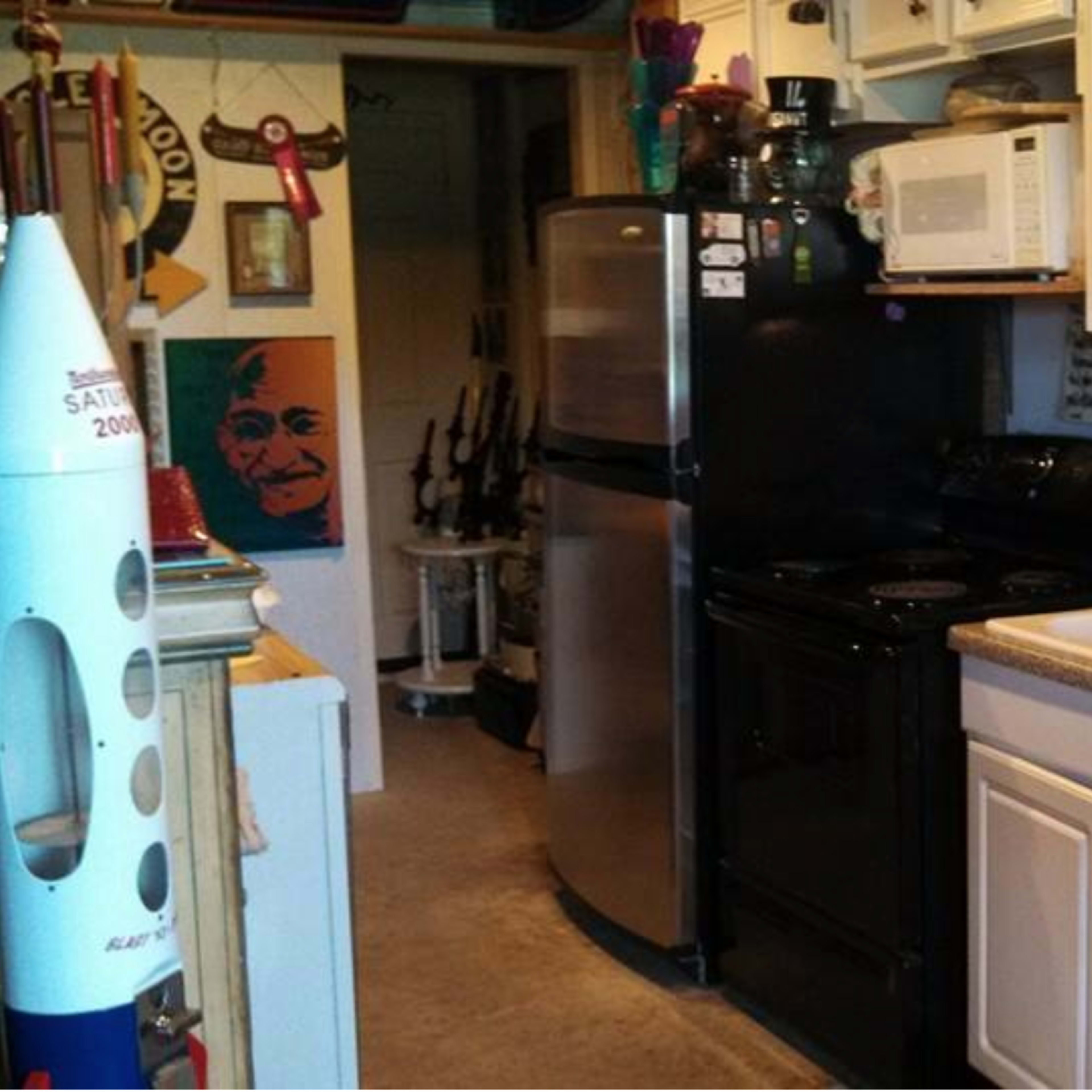 A compact kitchen featuring black appliances, a dual sink, and white cabinetry, surrounded by various utensils and decorations.